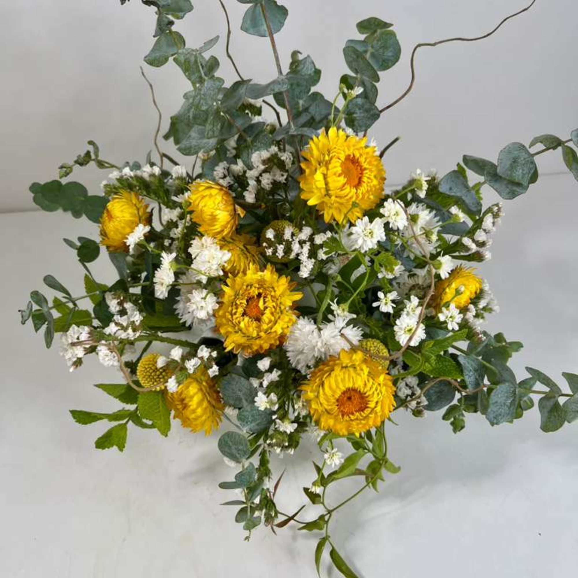 Yellow flowers with white filler and eucalyptus in a loose bouquet
