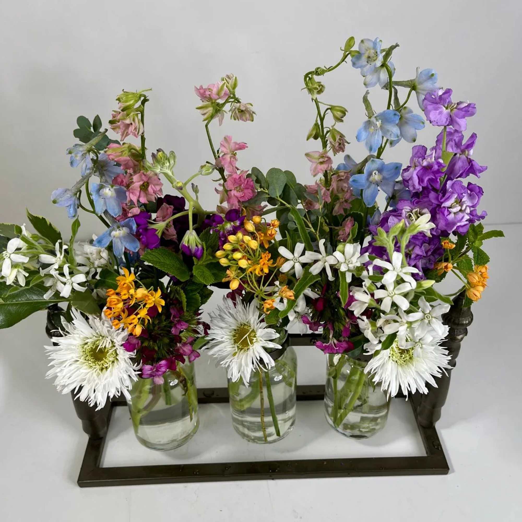 Mixed flowers arranged in three glass jars on a tray