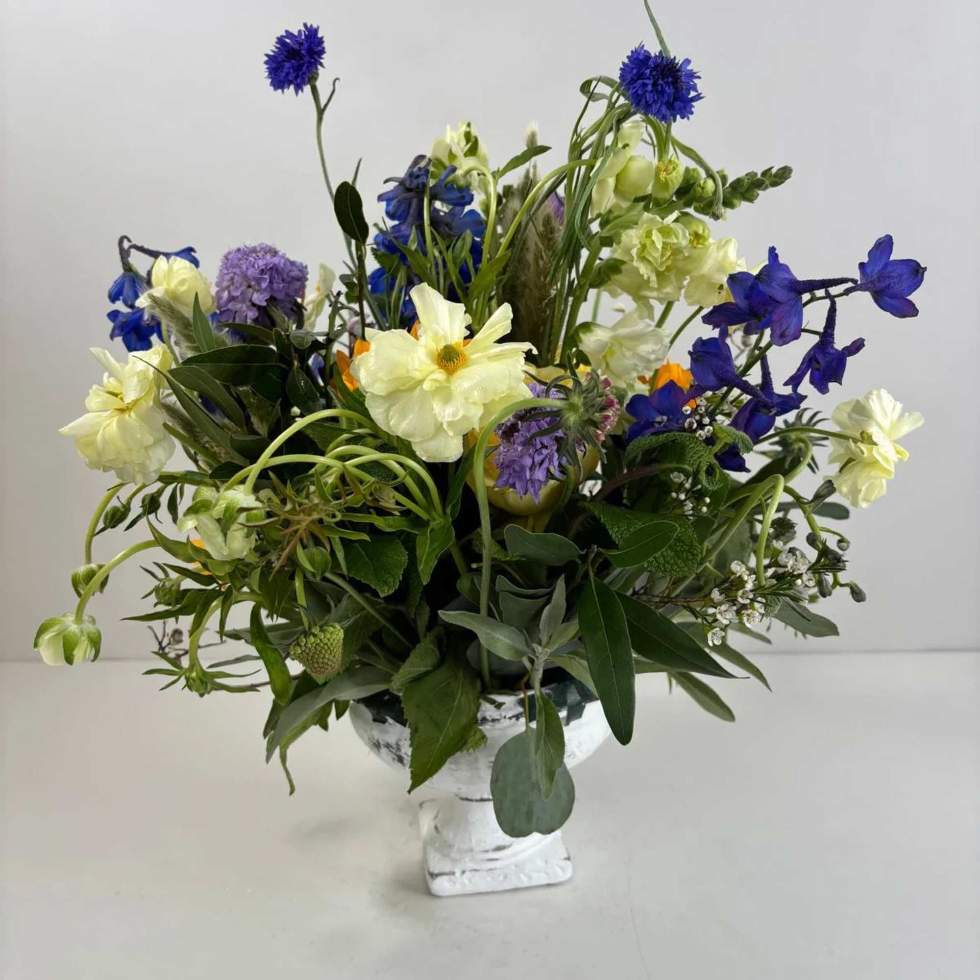 Mixed blue, white, and purple flower arrangement in a white pedestal vase