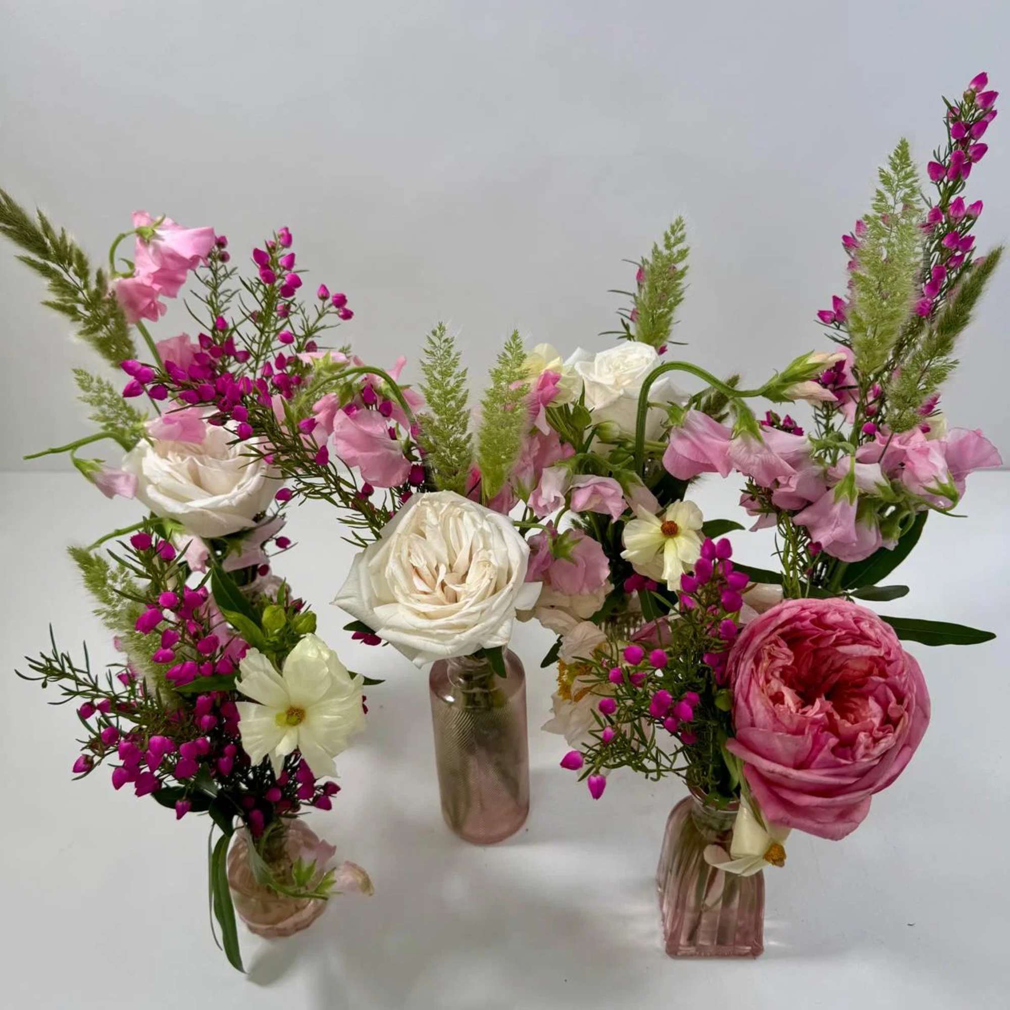 Three small floral arrangements in glass vases with pink and white blooms