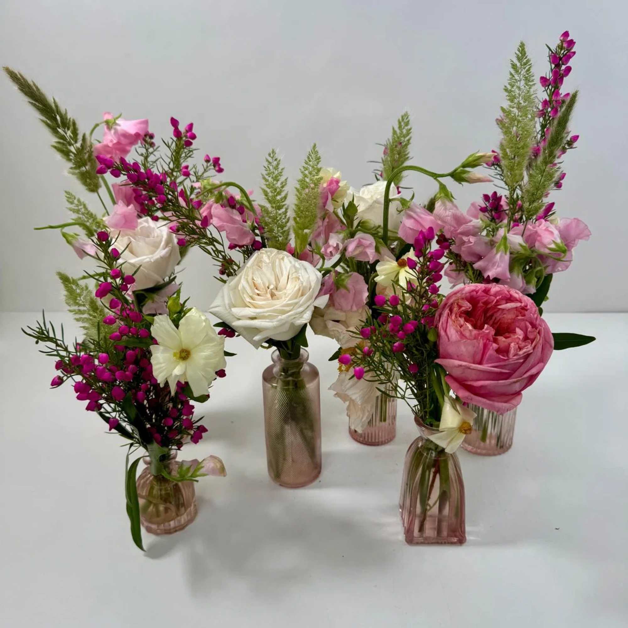 Assorted pink and white floral arrangements in small glass vases