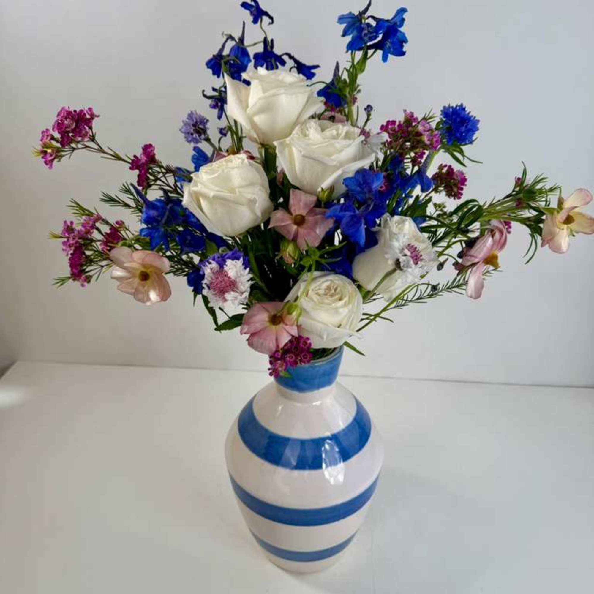 White roses and blue flowers arranged in a striped vase