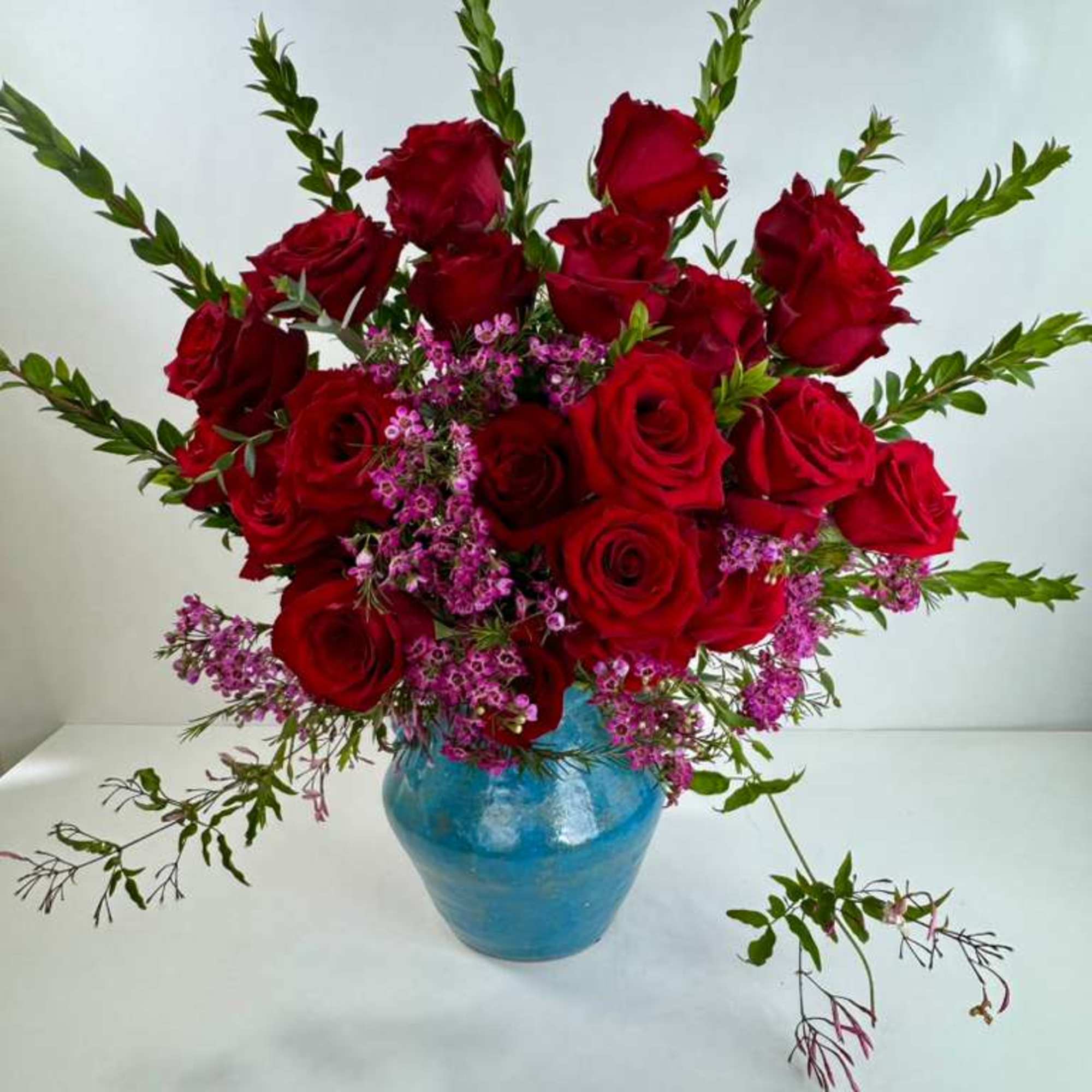 Red roses arranged in a blue vase with small purple filler flowers
