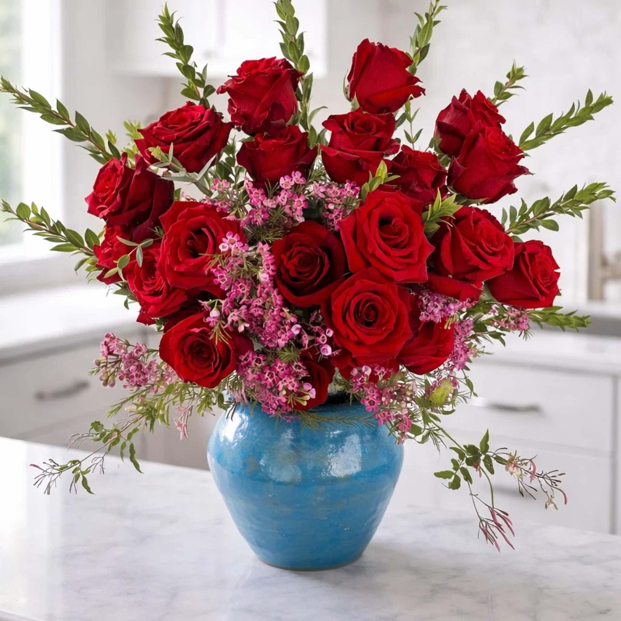 Red roses arranged in a blue vase with pink filler flowers