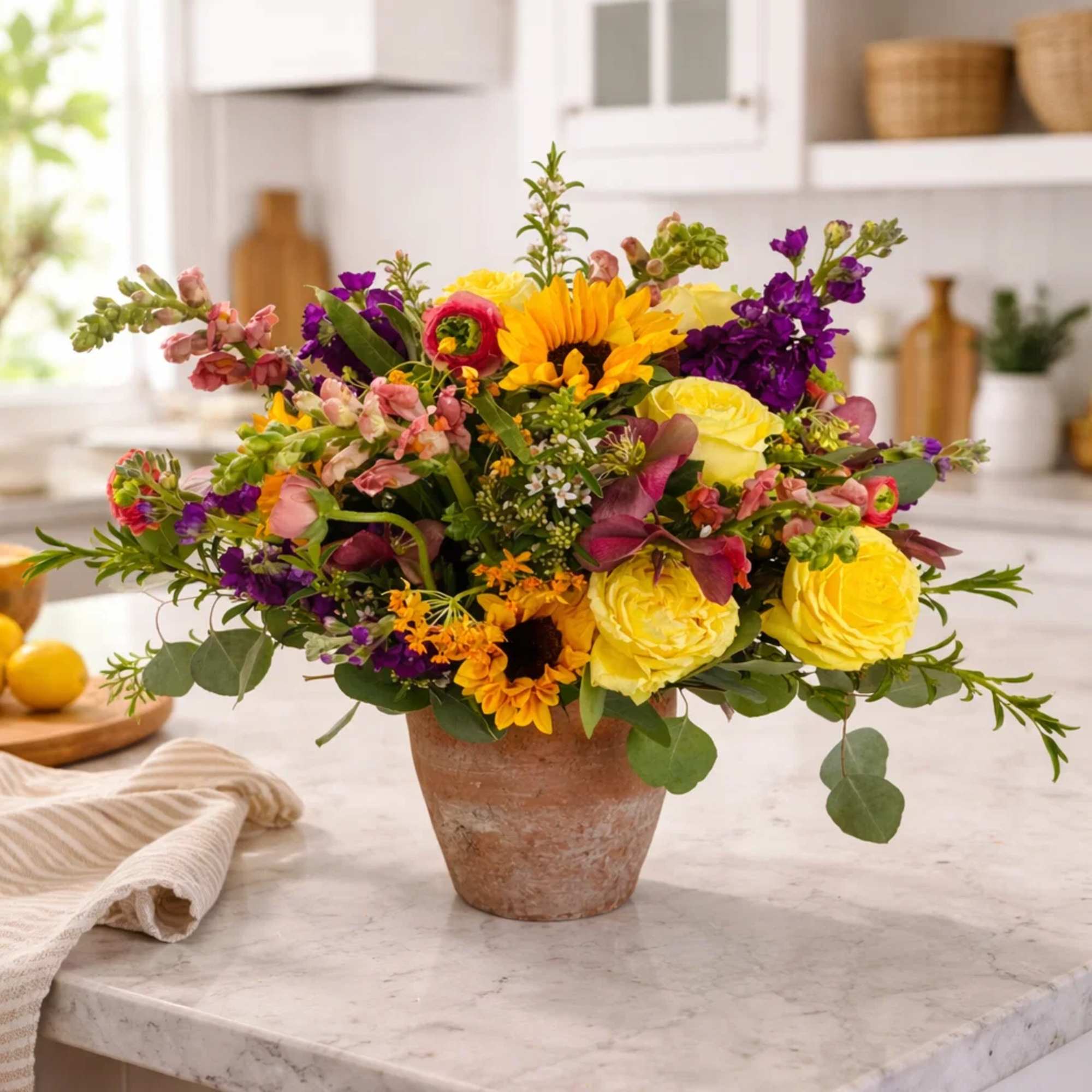 Colorful mixed flower arrangement in a terracotta pot on a kitchen counter