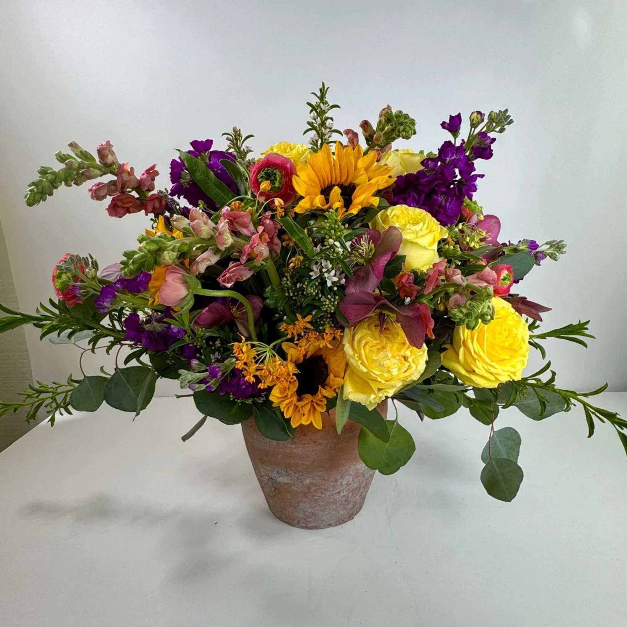 Mixed bouquet with yellow roses, sunflowers, and purple blooms in a rustic vase