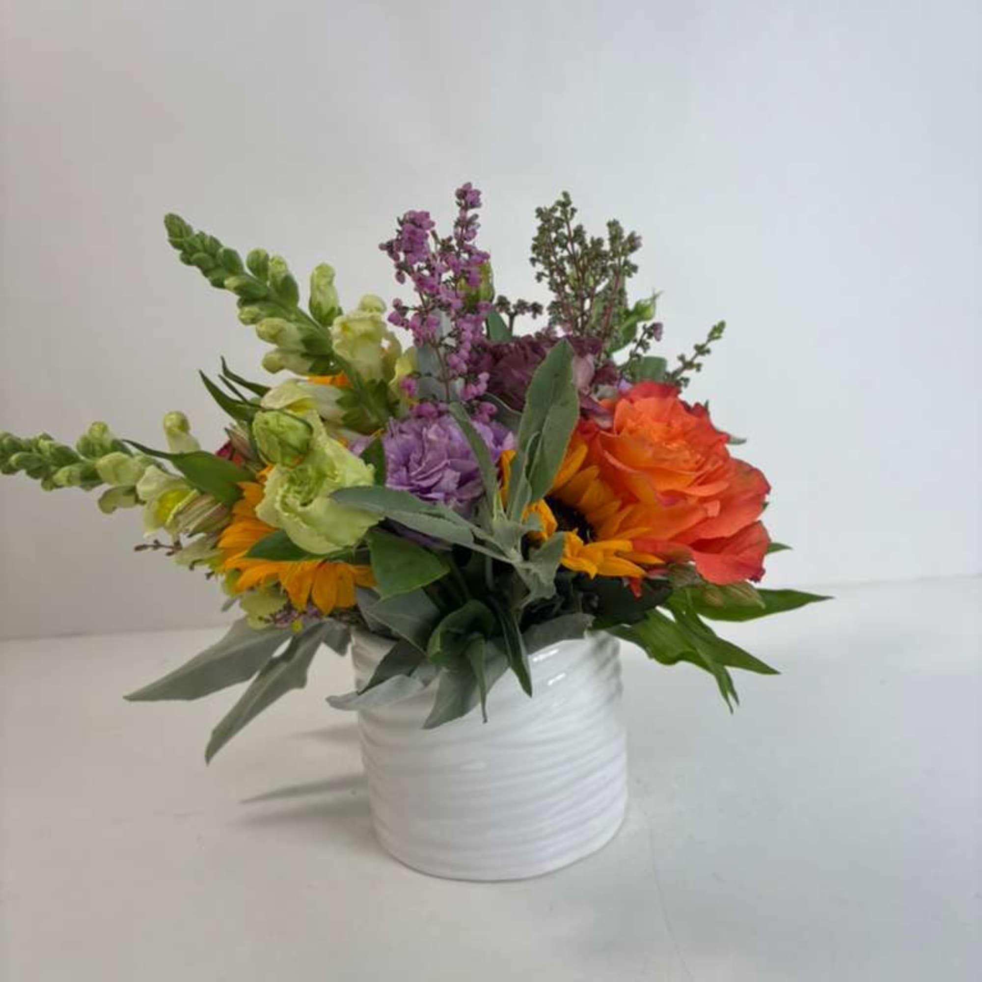 Mixed bouquet in a white vase with orange, purple, and green blooms