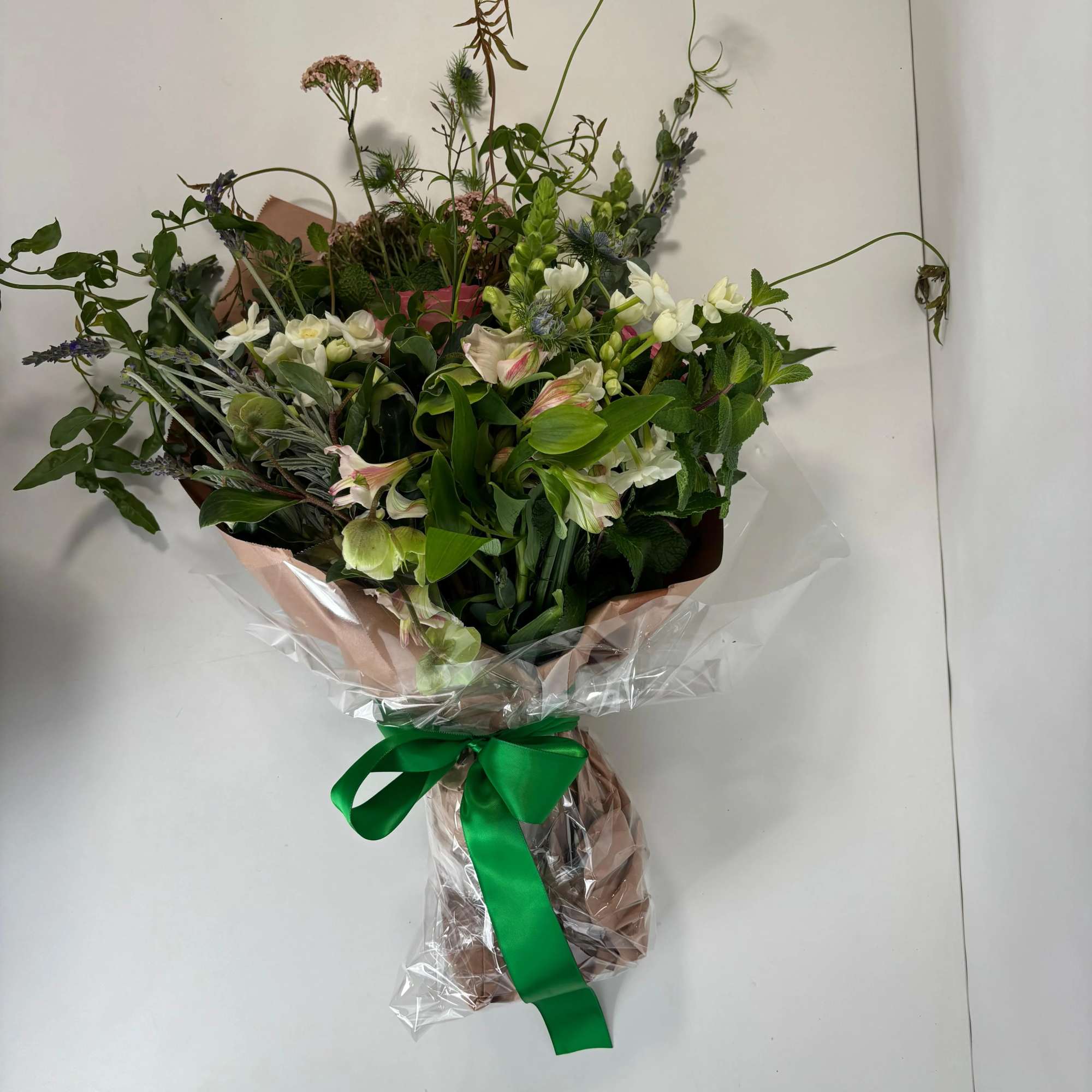 Hand-tied bouquet of mixed white and pink flowers wrapped in paper with a green ribbon