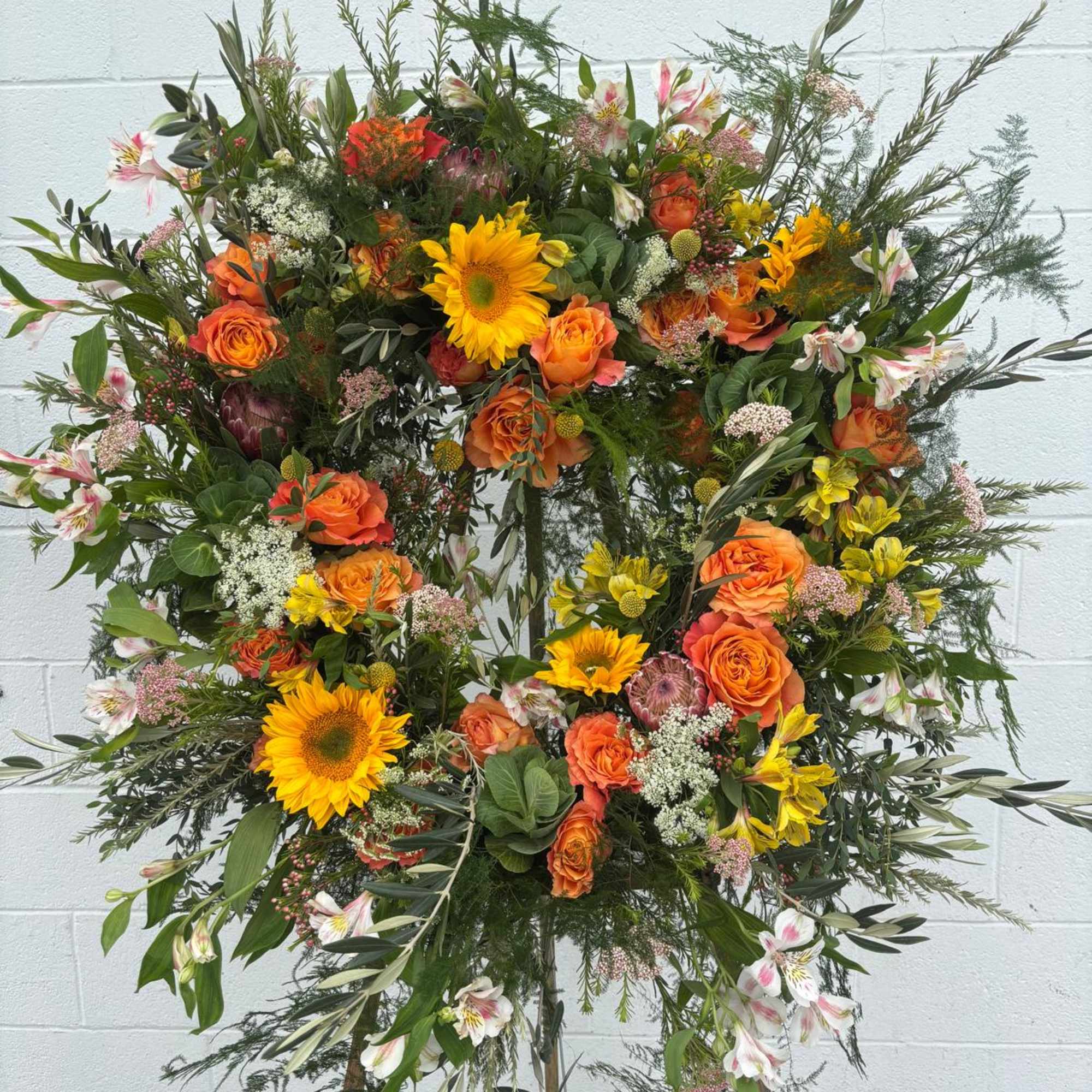 Large floral wreath on an easel with orange roses and yellow sunflowers