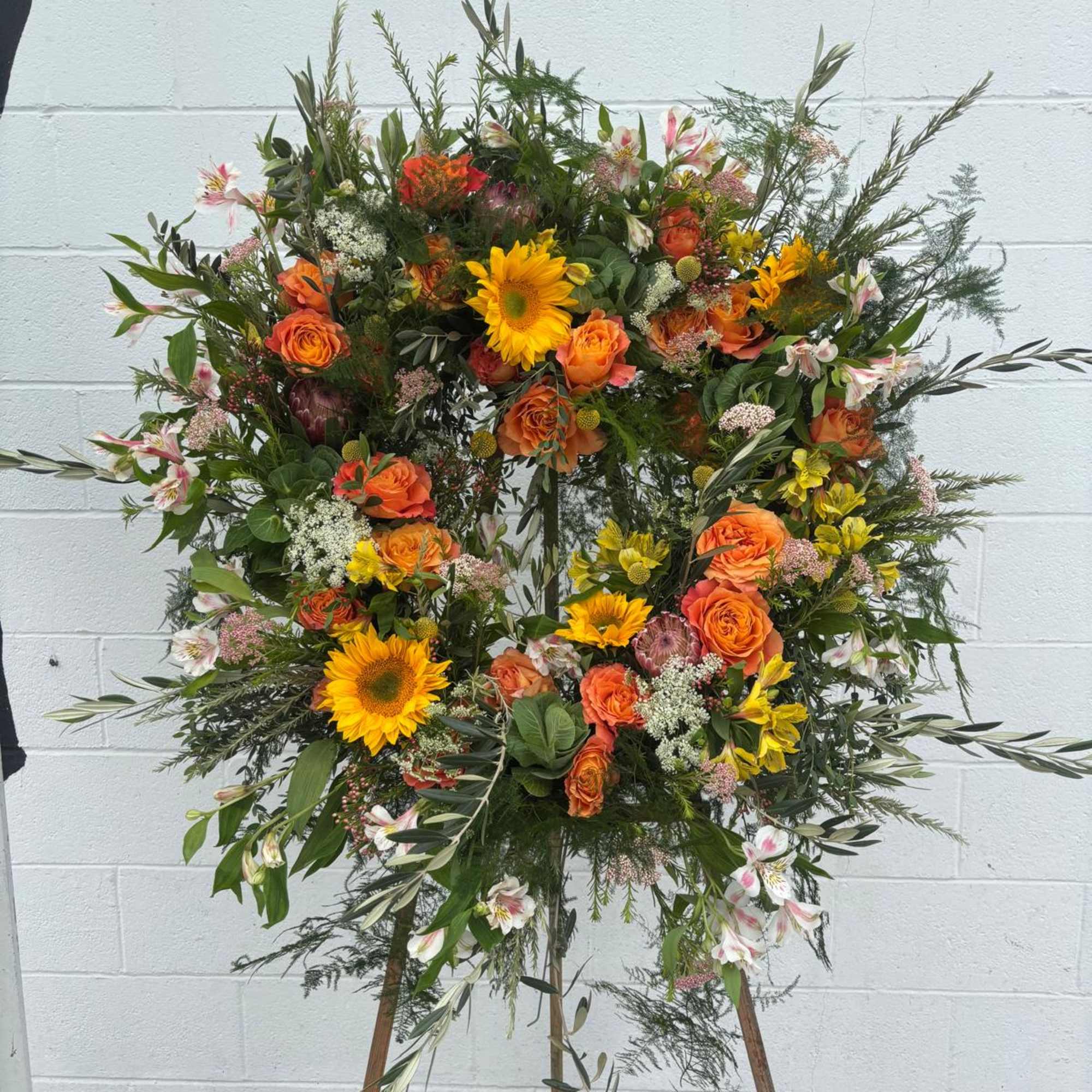Large floral wreath on a wooden easel with orange and yellow blooms