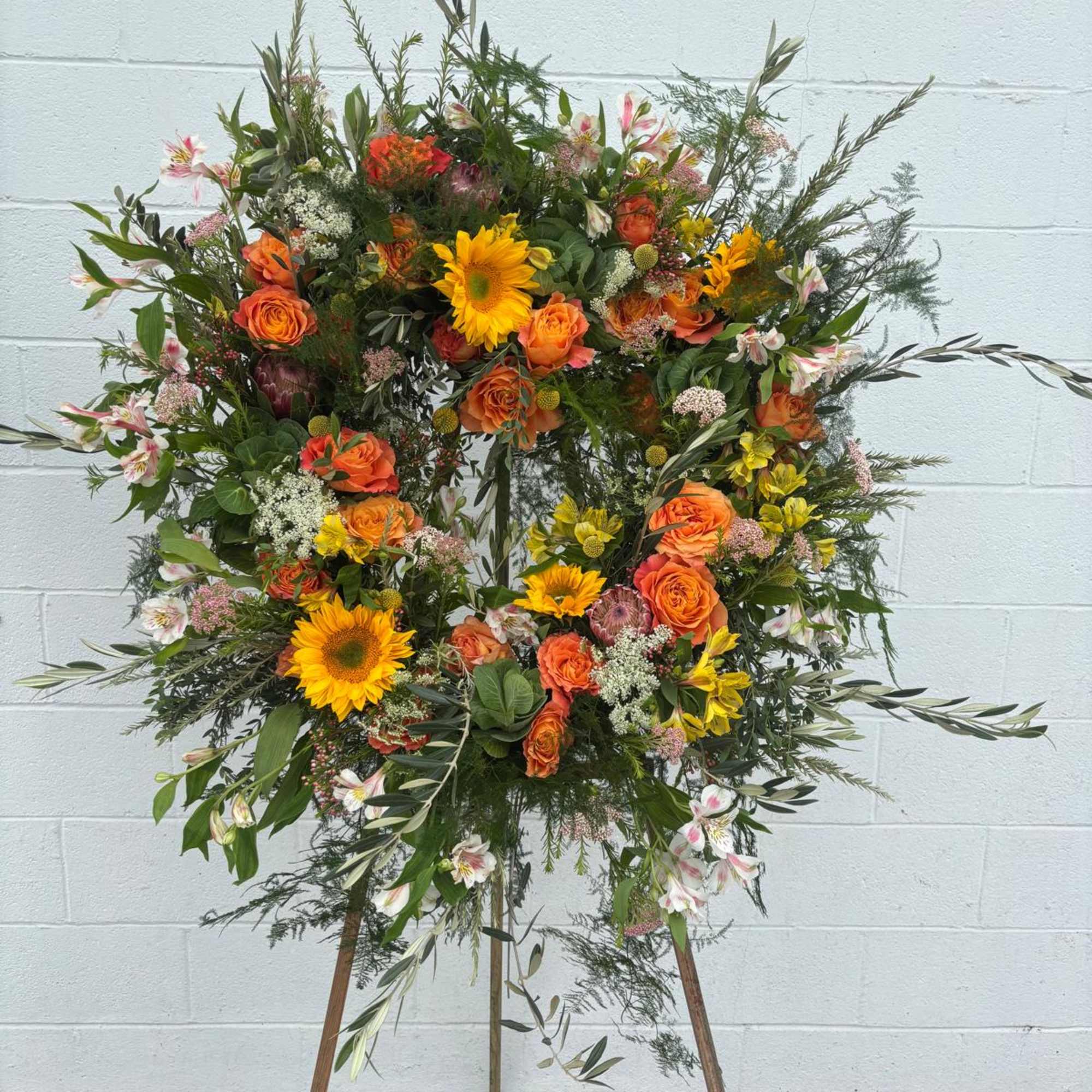 Large floral wreath on a stand with orange roses and yellow sunflowers