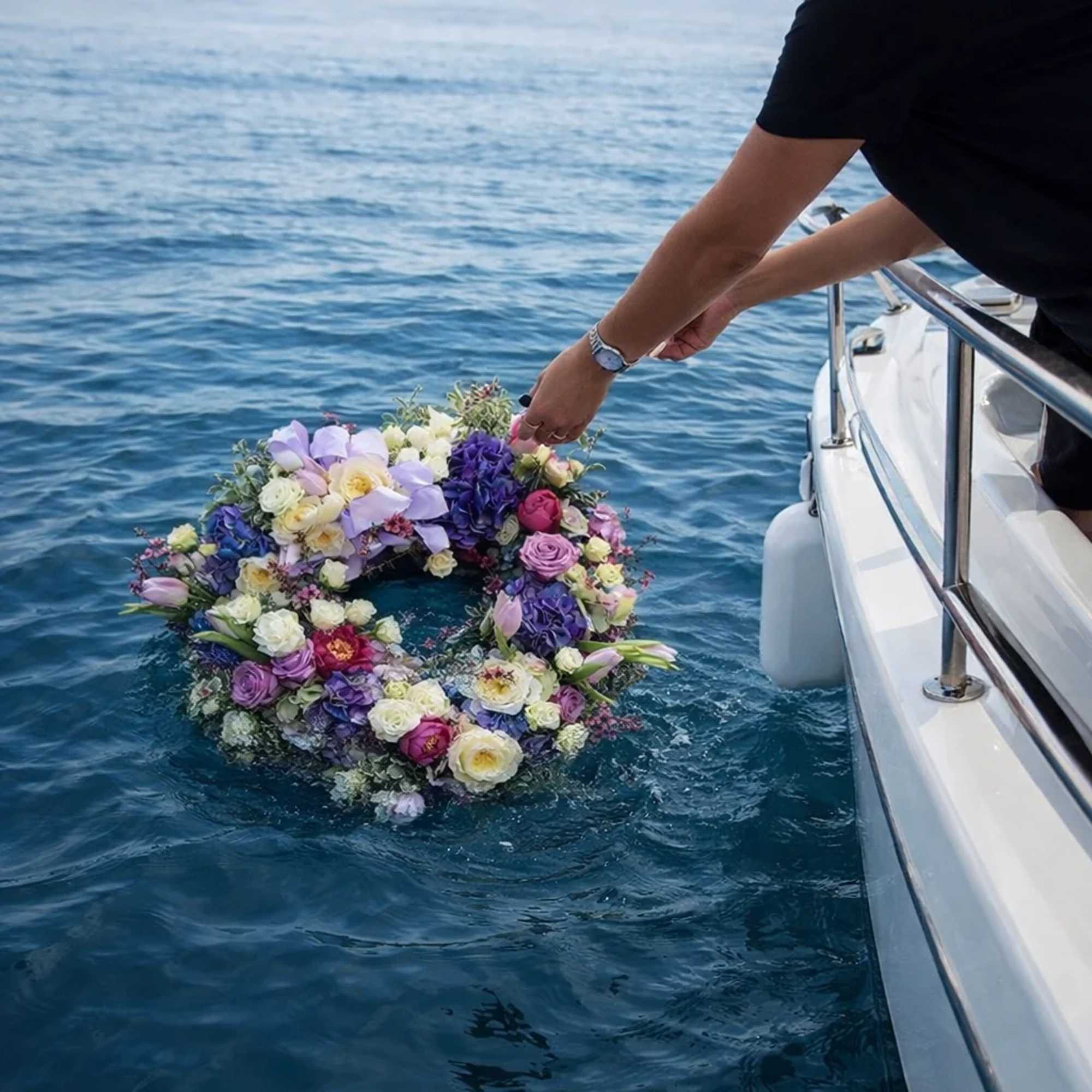 Person placing a circular flower wreath on the water beside a boat