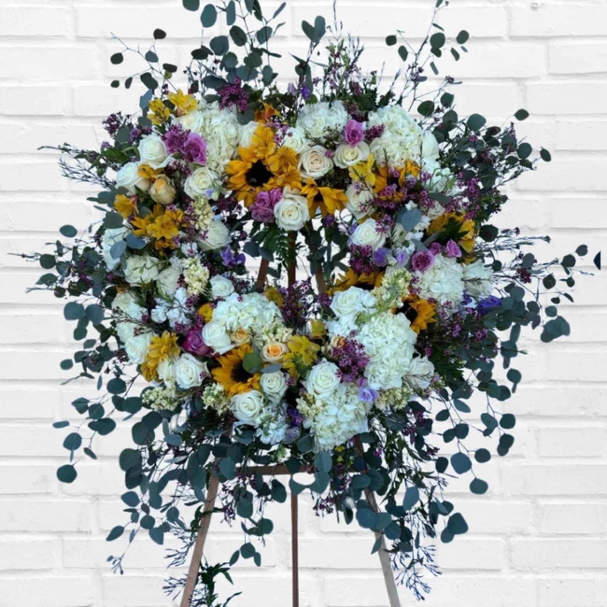 Large floral wreath on an easel with white, yellow, and purple flowers