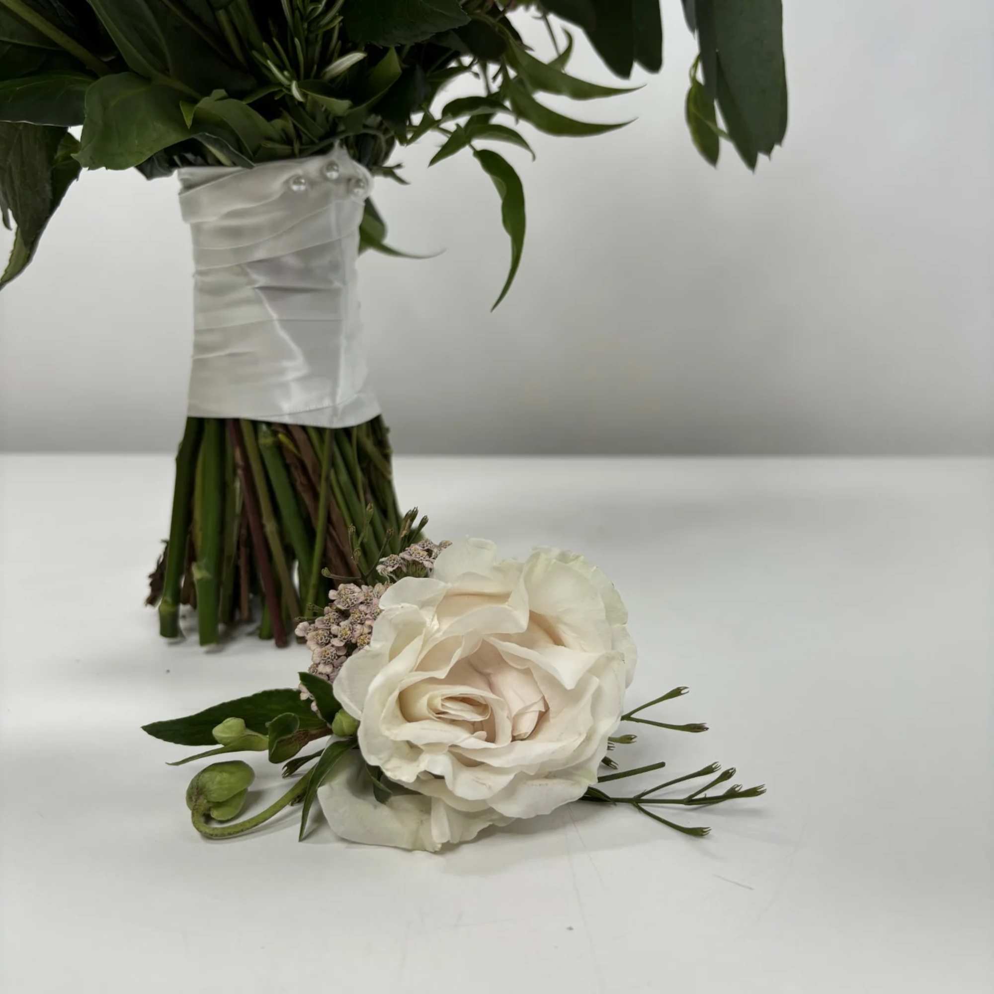 White rose boutonniere with small filler flowers and greenery