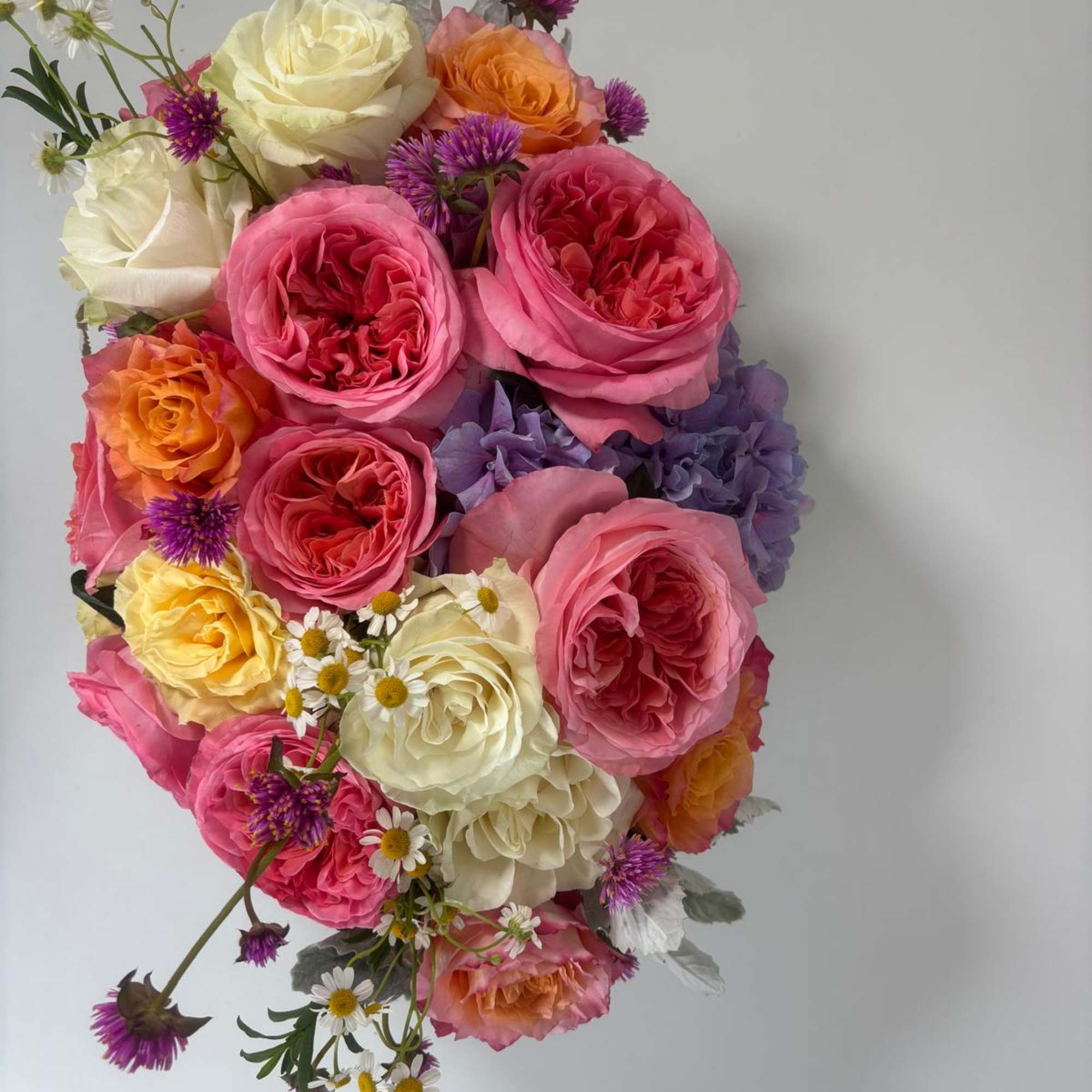 Bouquet of pink, cream, and orange roses with small purple and white accent flowers