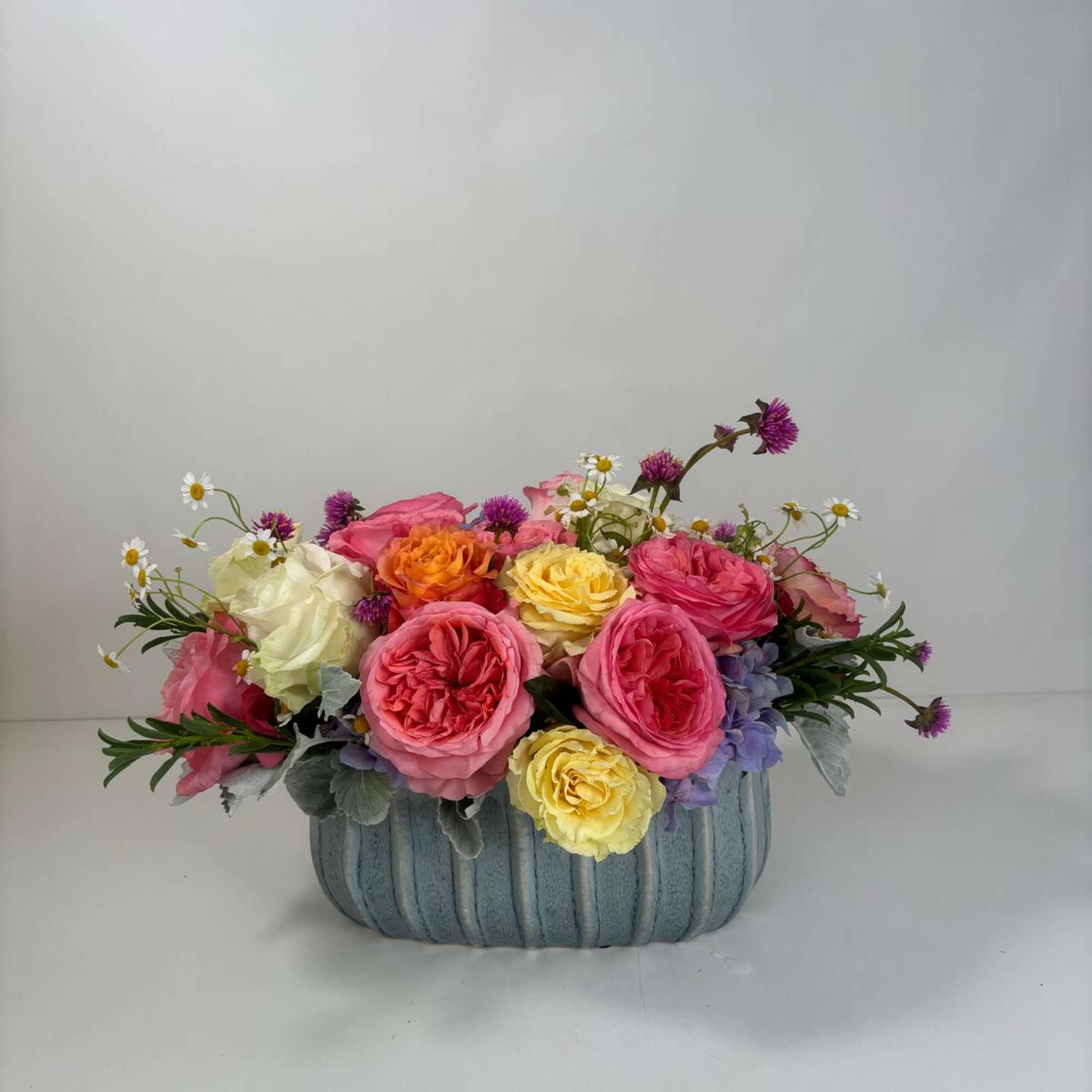 Mixed pink, yellow, and orange roses in a blue ribbed container