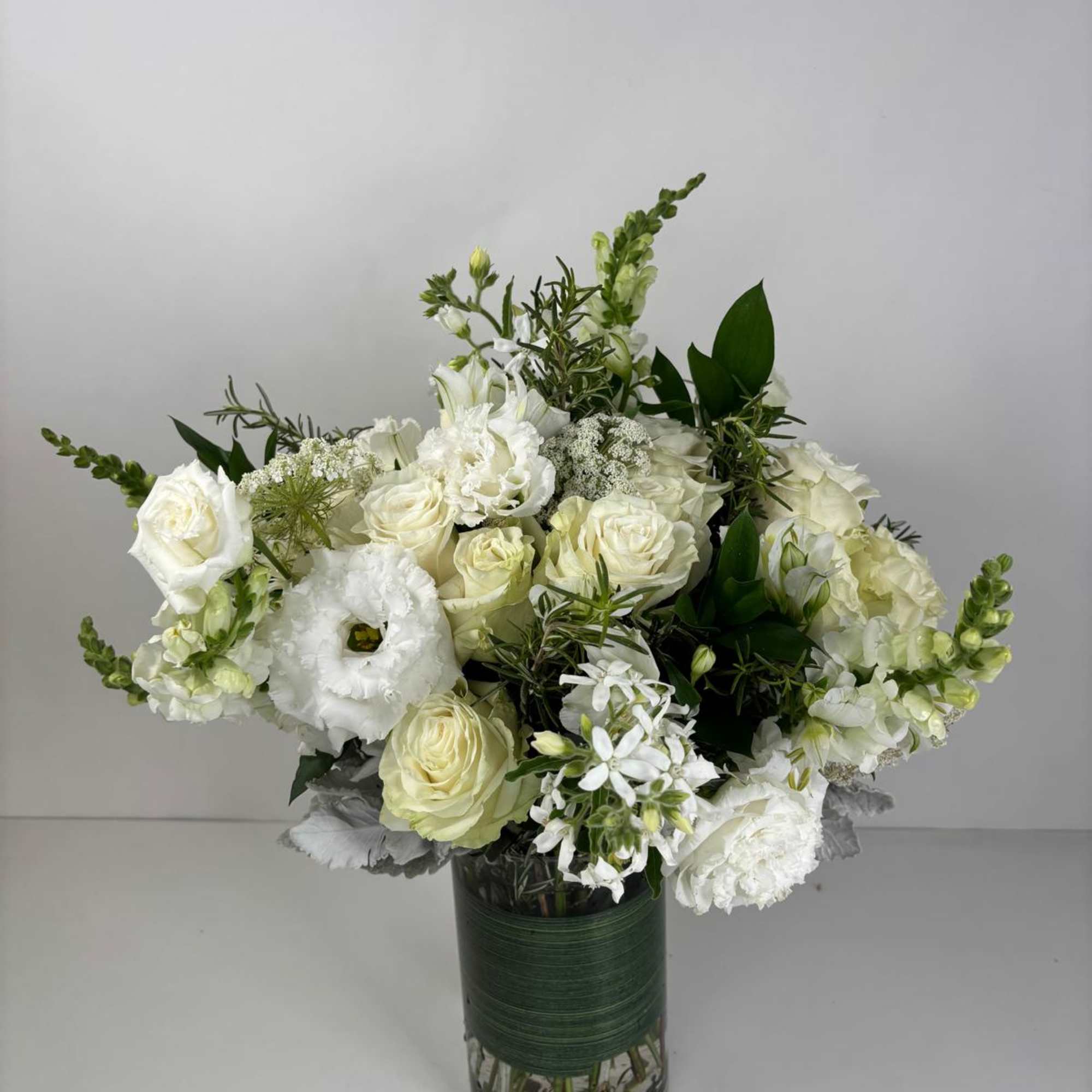 White floral arrangement in a glass vase with roses and snapdragons