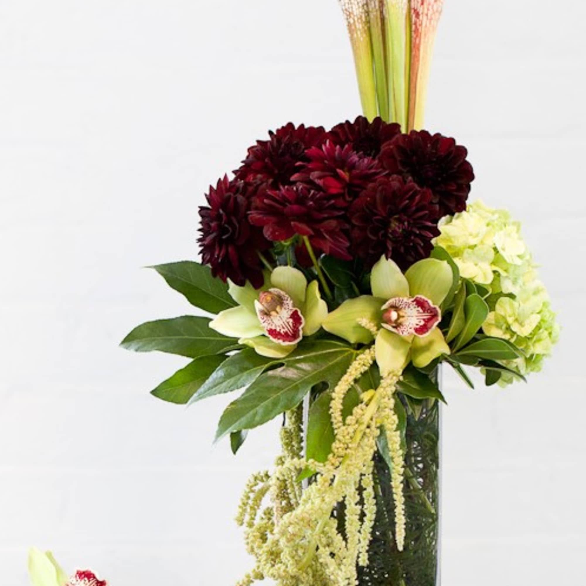 Tall floral arrangement in a glass vase with dark red blooms and pale orchids