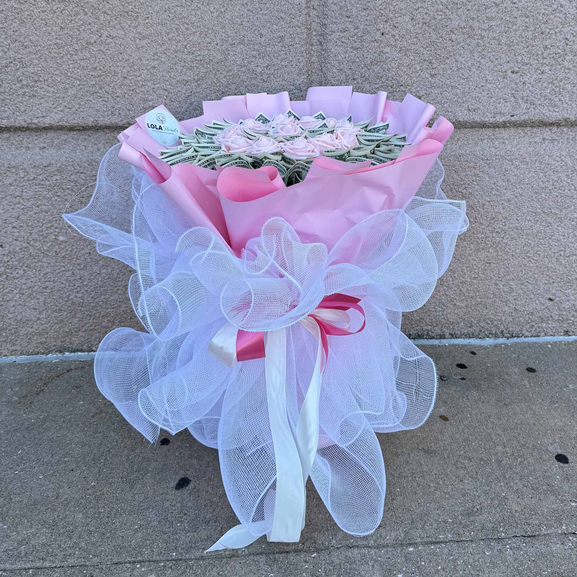 Pink bouquet wrapped in tulle with folded dollar bills and pale roses
