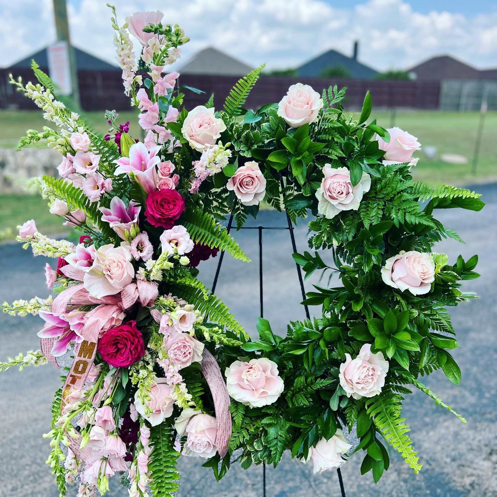 Pink and white floral wreath on a black stand outdoors