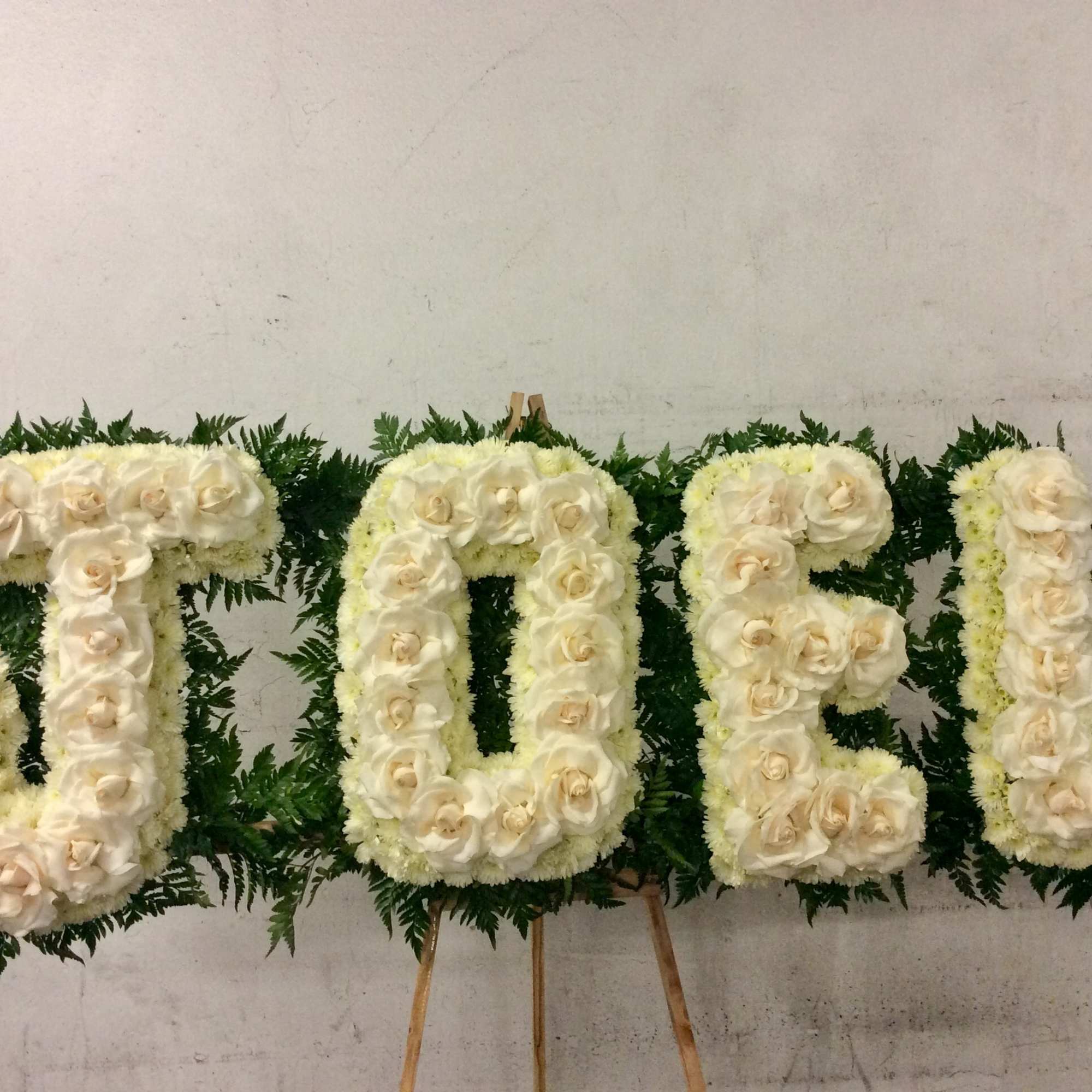 Floral tribute spelling "TIDE" in white roses and greenery.