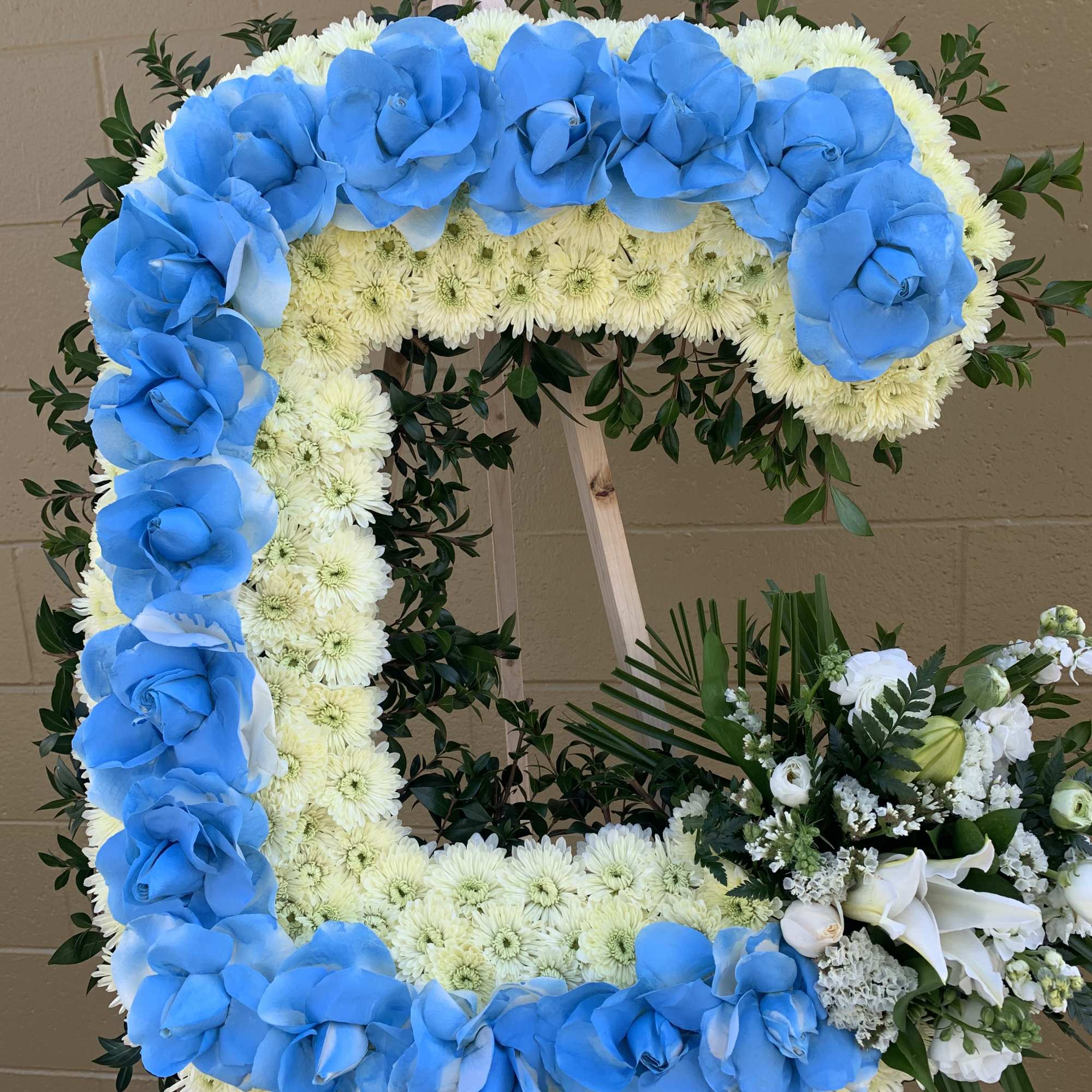 Square floral wreath with blue roses and white chrysanthemums on an easel