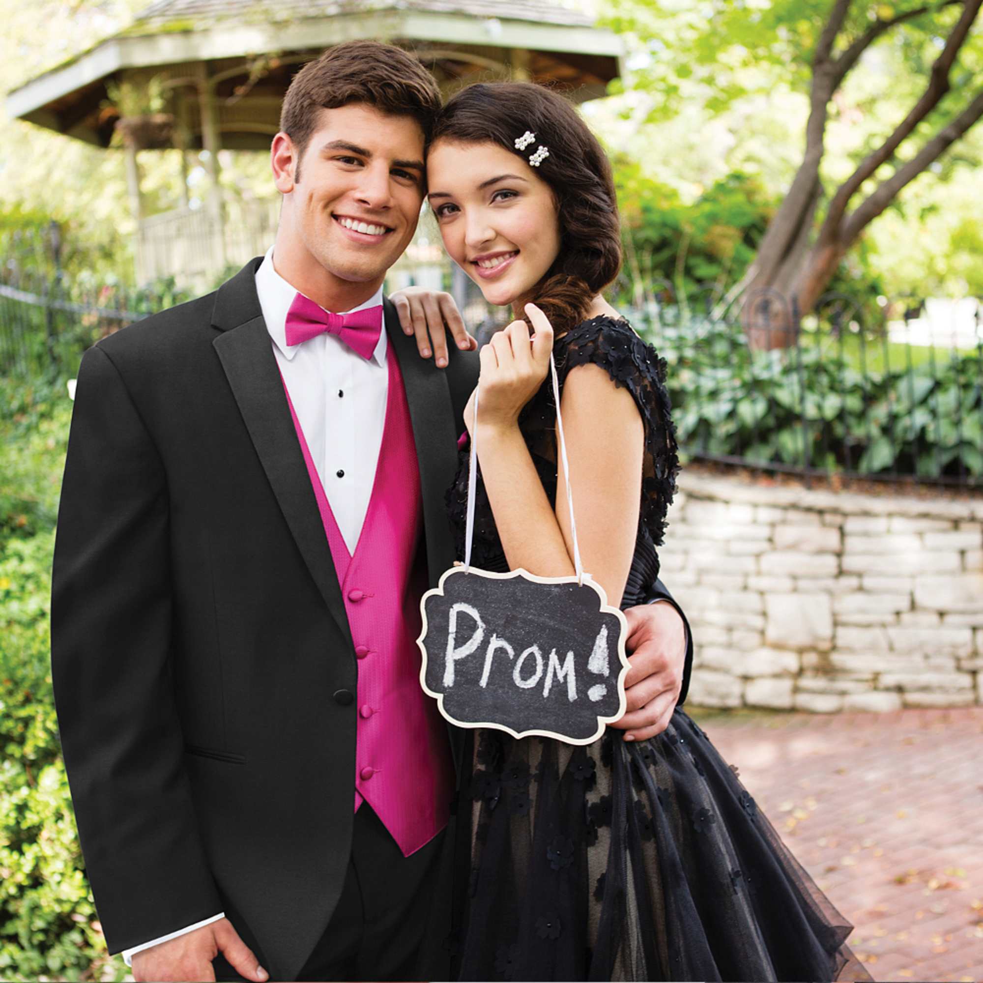 A young couple dressed for prom holds a chalkboard sign.