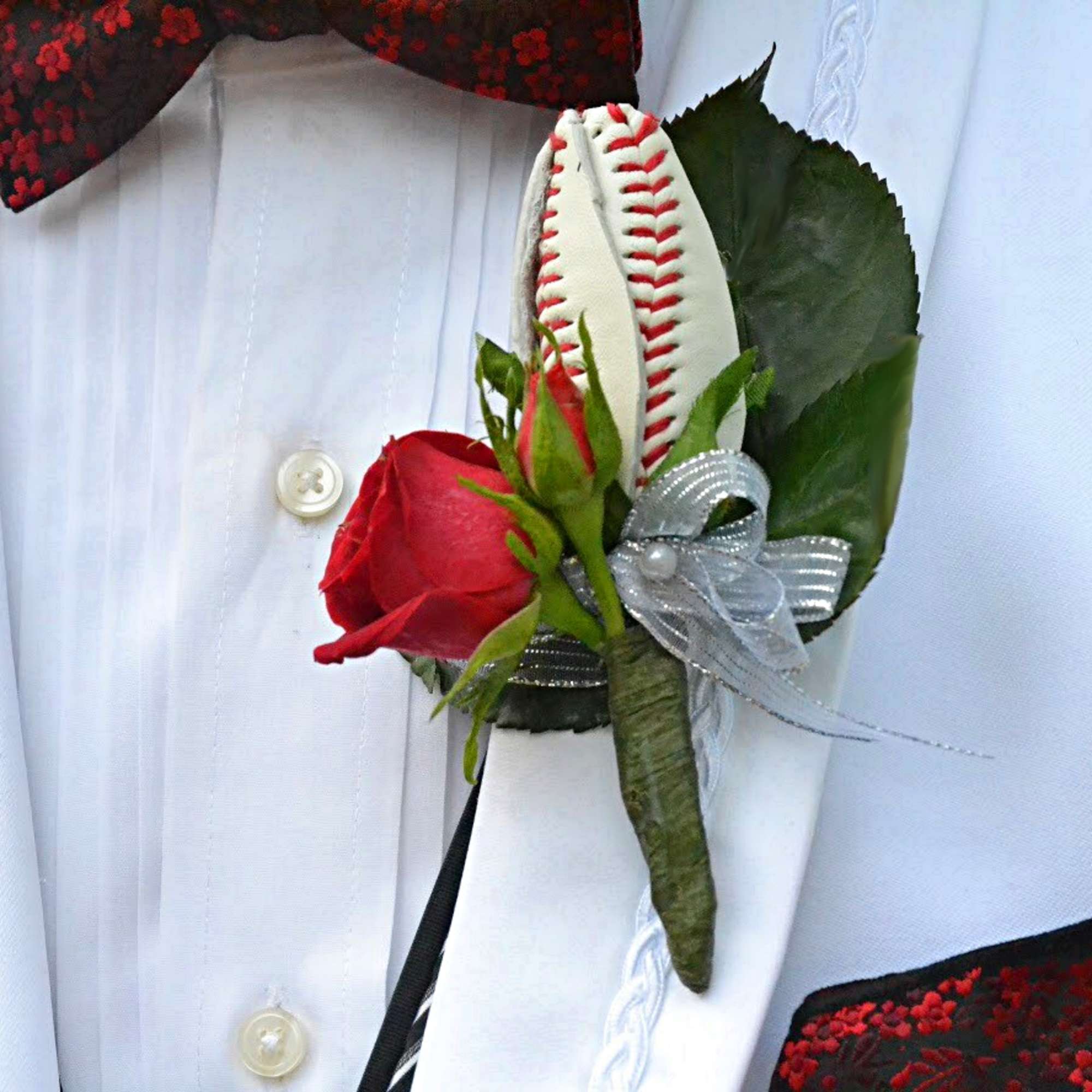 Red rose boutonniere with a baseball accent and silver ribbon on a white shirt