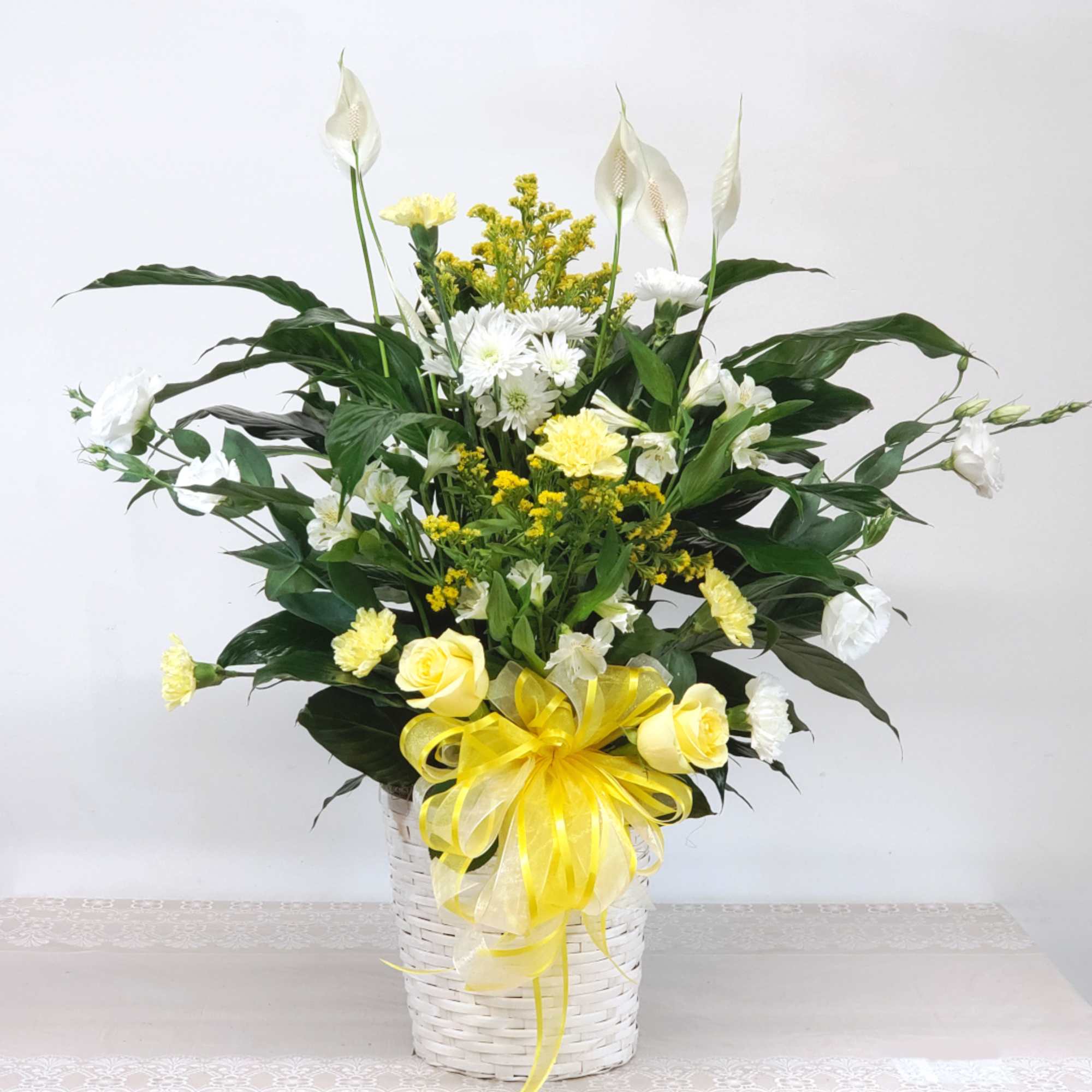 White and yellow floral arrangement in a white basket with a yellow bow