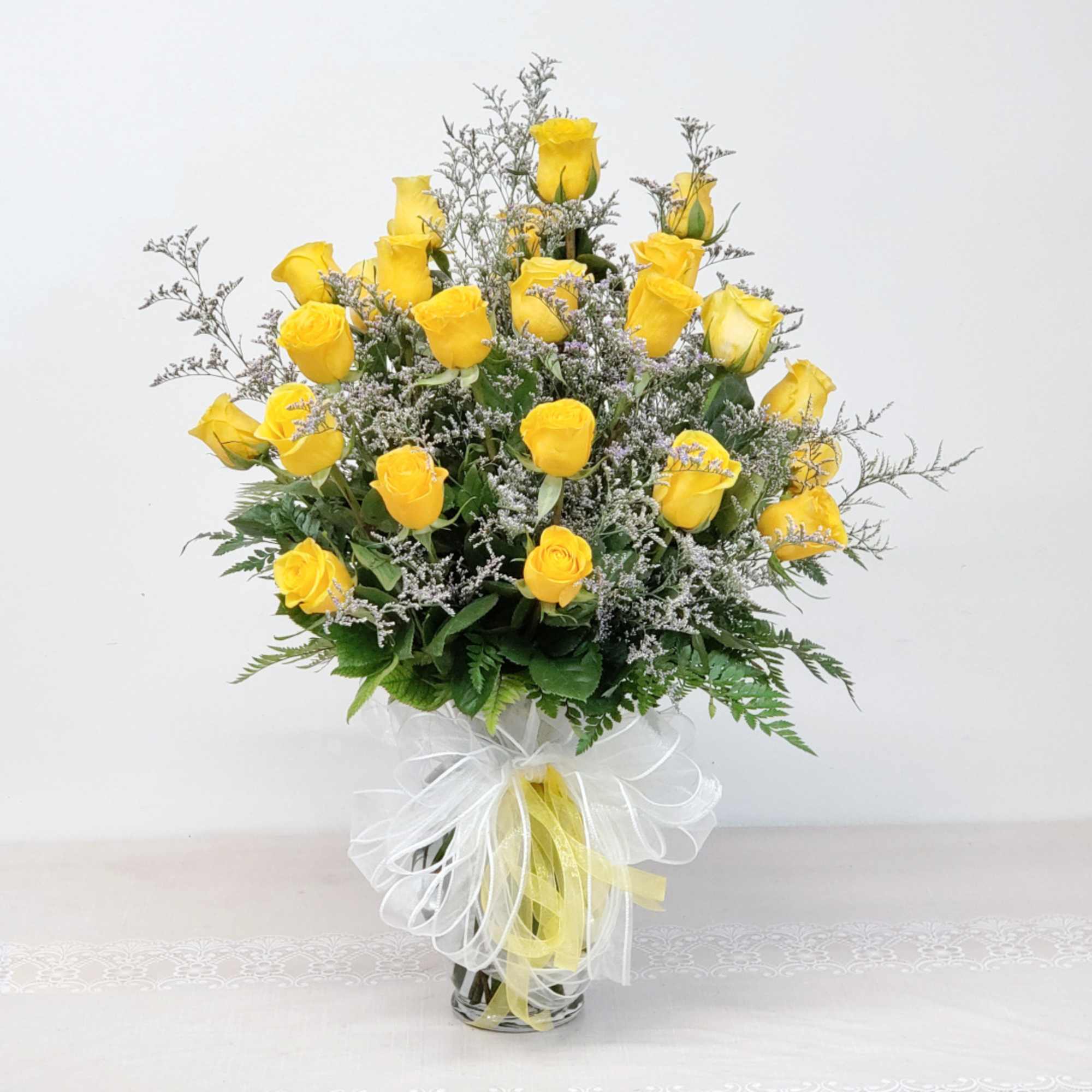Yellow roses arranged in a clear glass vase with a white ribbon bow