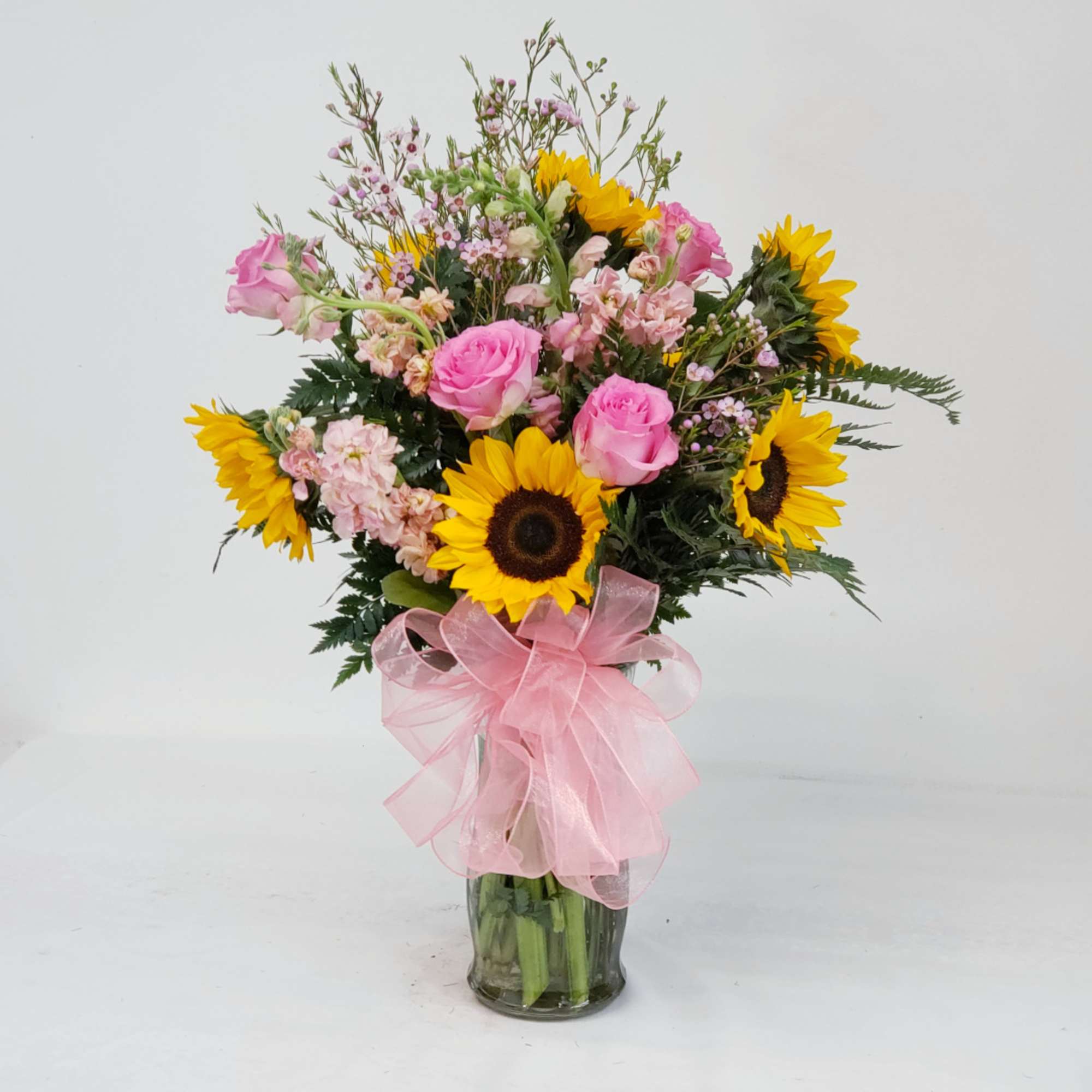 Bouquet of pink roses and sunflowers in a glass vase with a pink ribbon
