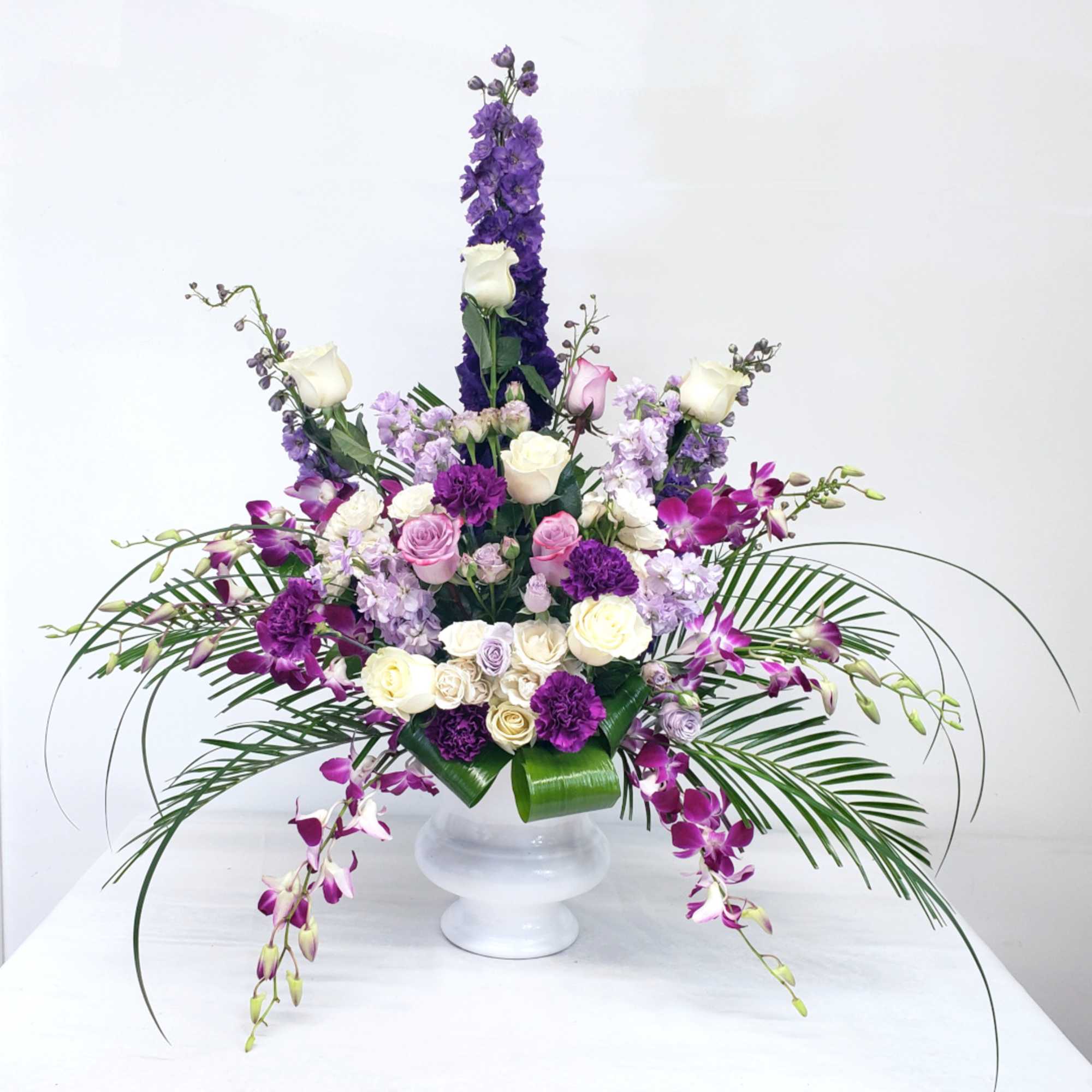 Large purple and white floral arrangement in a white pedestal vase
