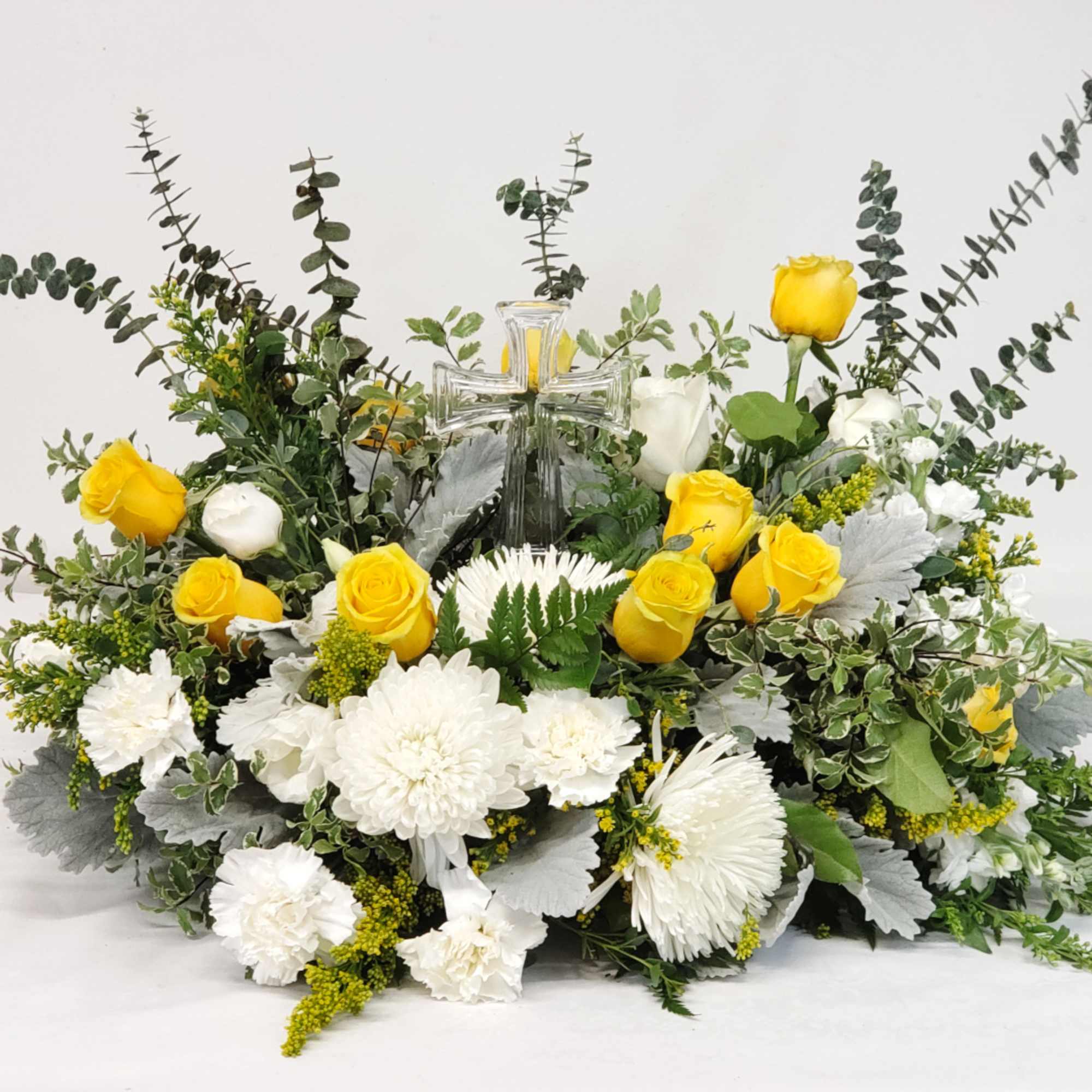 Yellow roses and white flowers arranged around a glass cross.