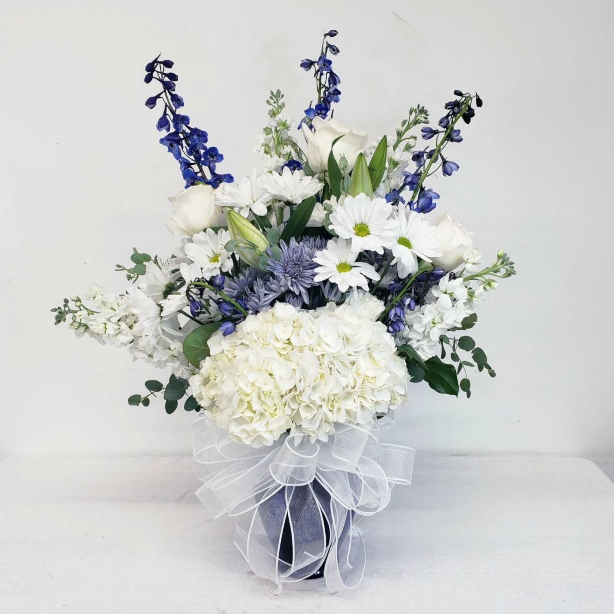 White and blue floral arrangement in a dark vase with a sheer ribbon bow