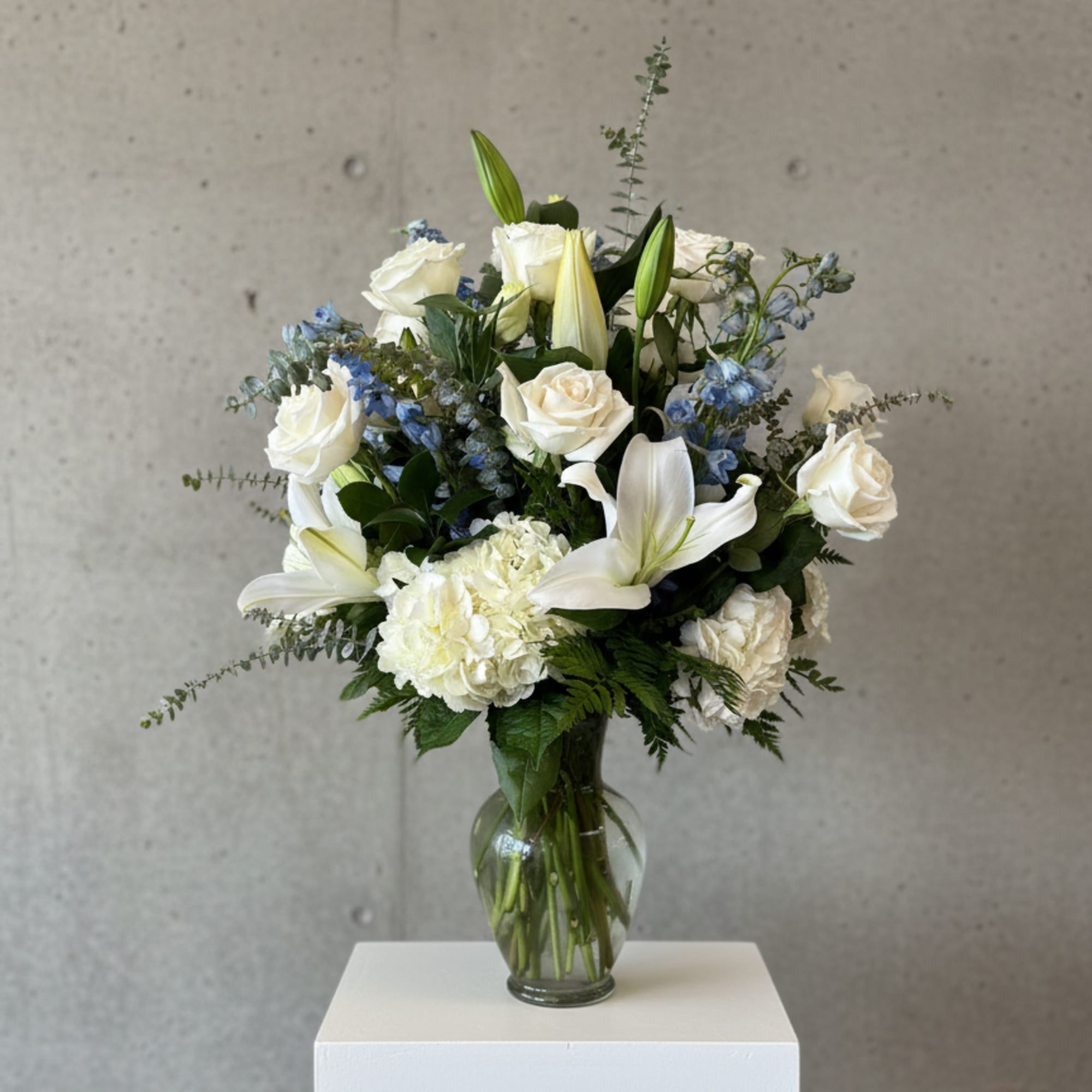 White roses and lilies arranged in a glass vase with blue accents.