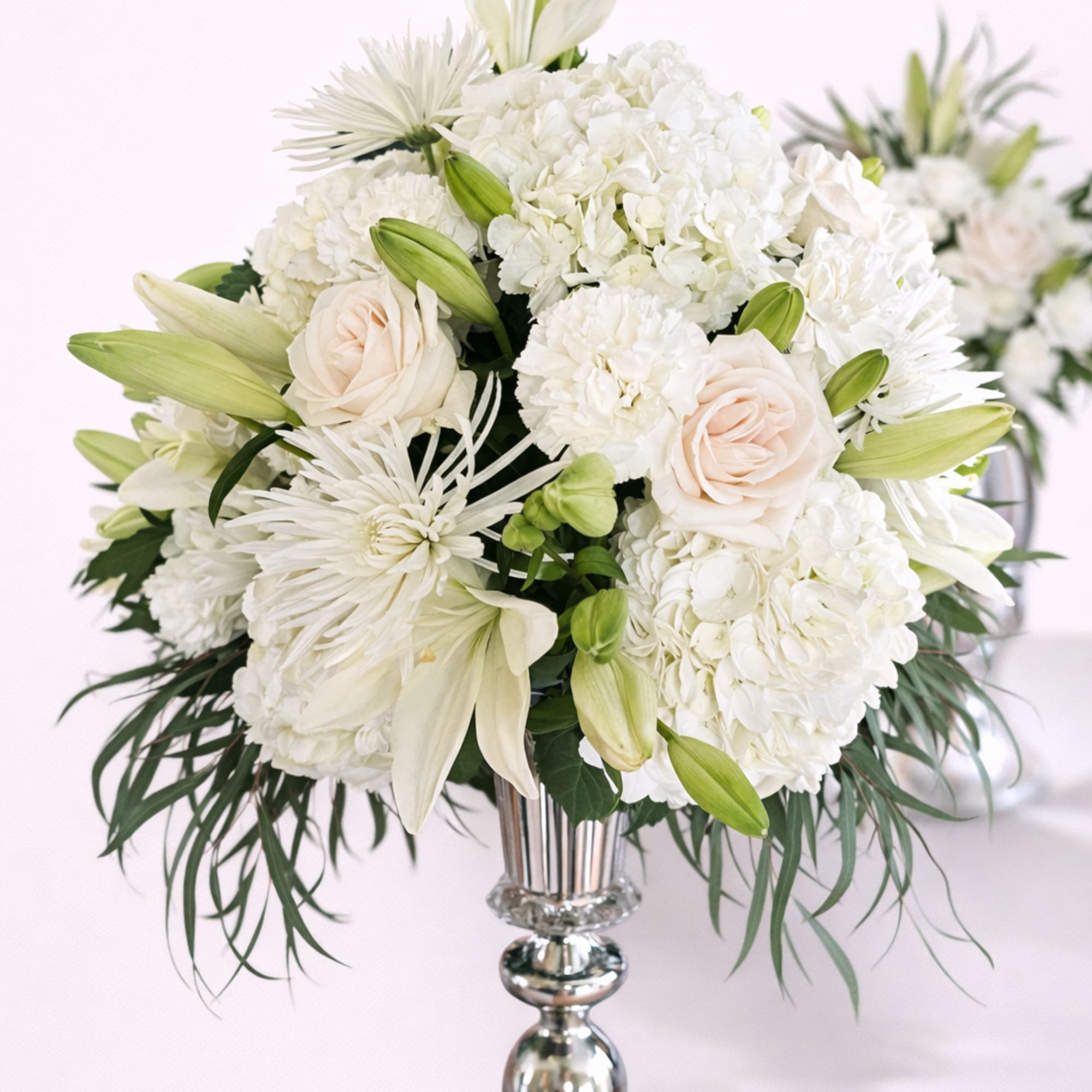 White floral arrangement in a silver vase with lilies and roses