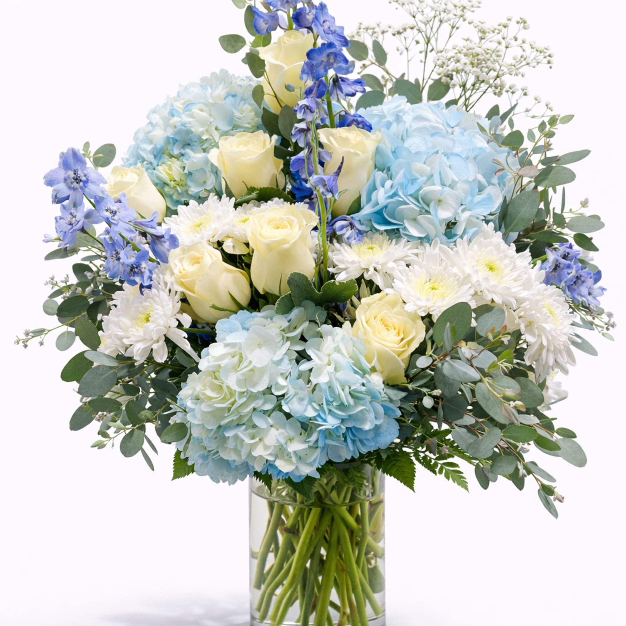 Blue hydrangeas, ivory roses and white mums in a clear glass cylinder vase
