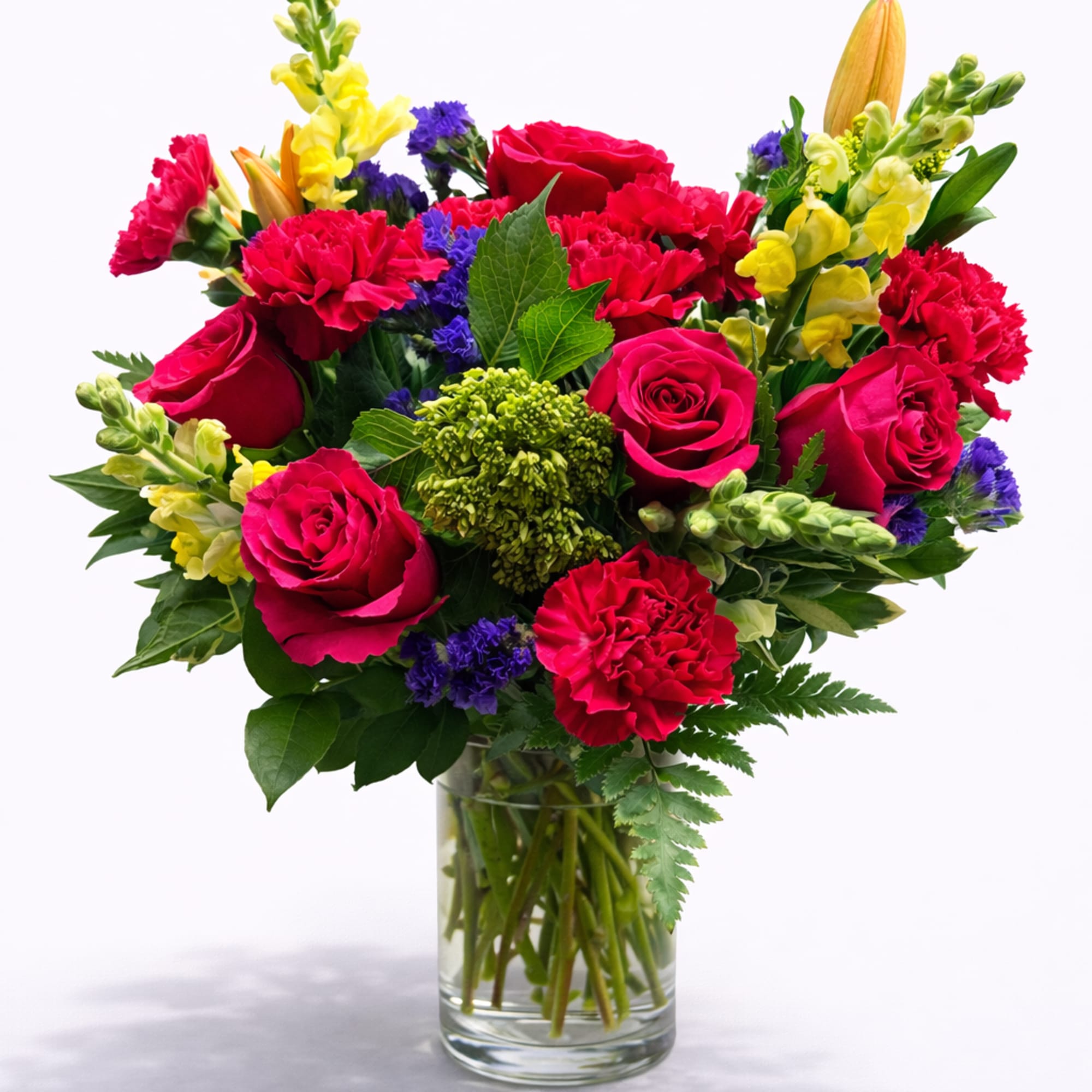 Mixed bouquet of red roses, pink carnations, and yellow snapdragons in a glass vase