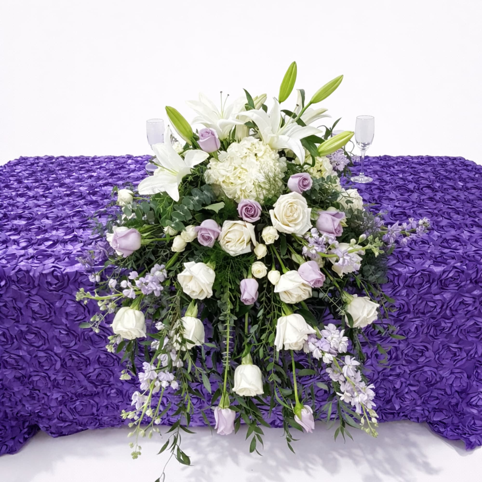White lilies and roses arranged on a purple floral-draped casket