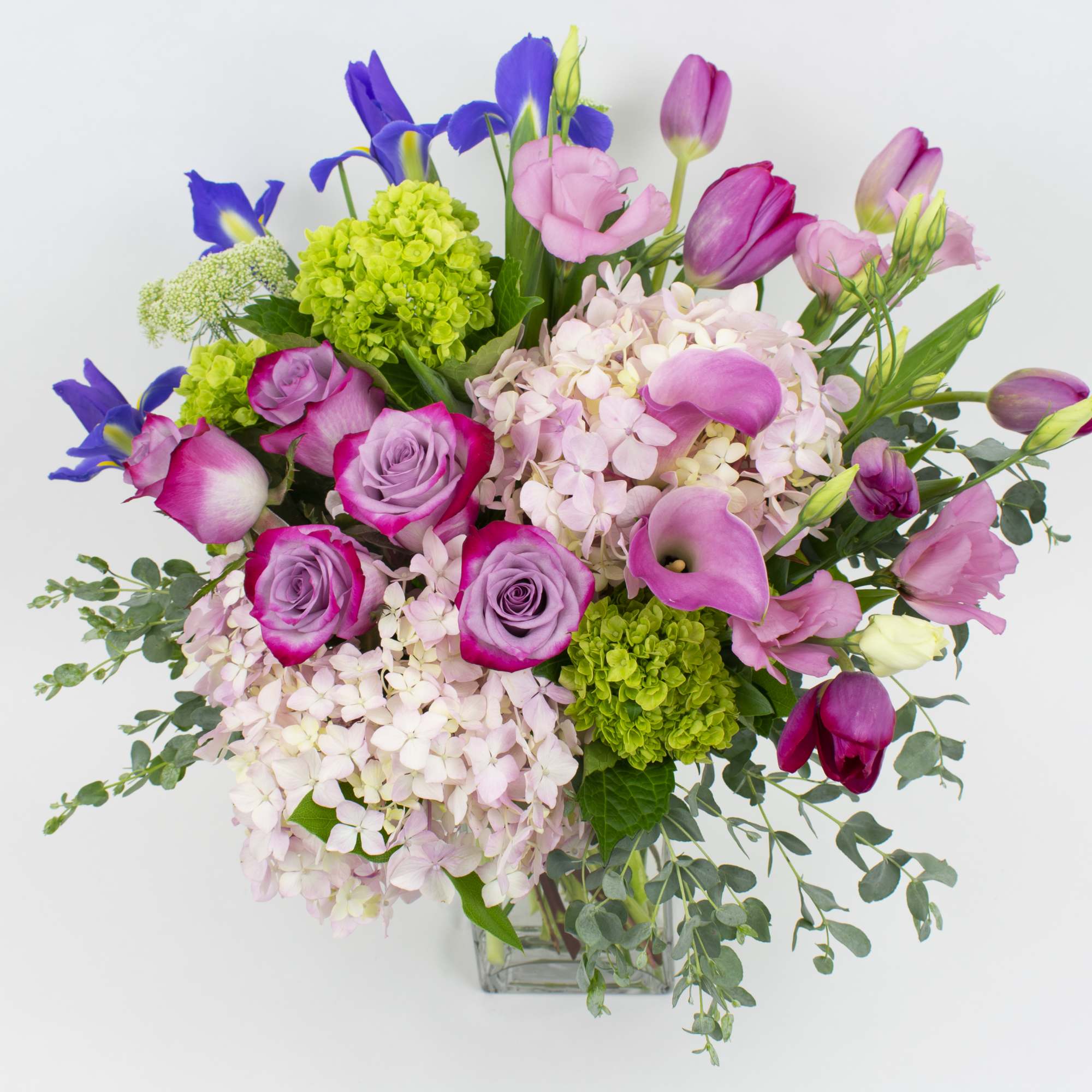 Mixed bouquet of pink roses, hydrangeas, and purple tulips in a clear vase