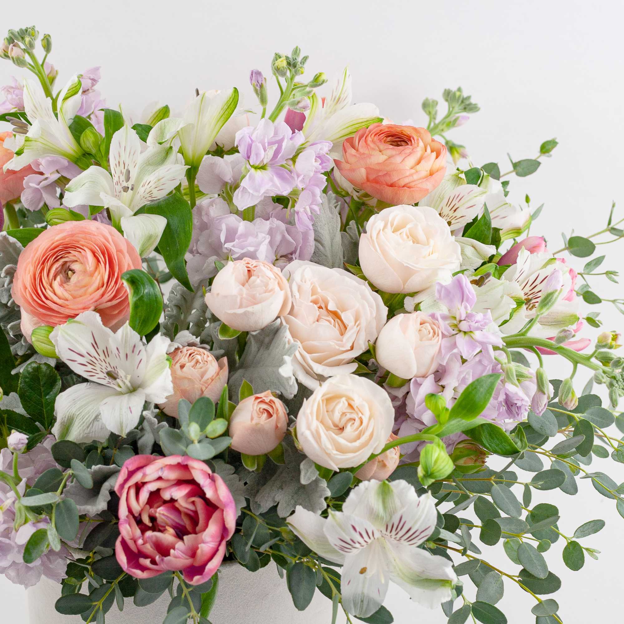 Bouquet of peach, pink, and white flowers with eucalyptus in a white container