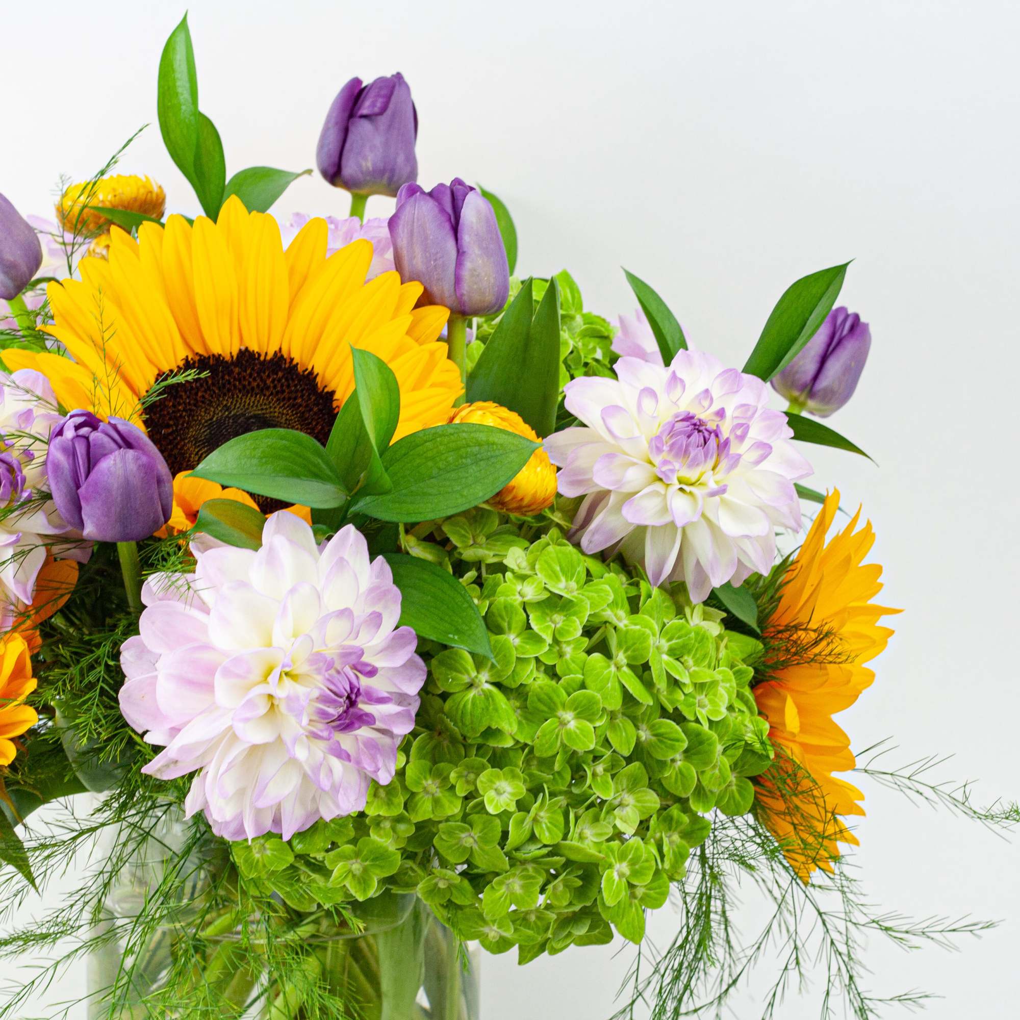 Bouquet of sunflowers, purple tulips, and pale dahlias in a glass vase
