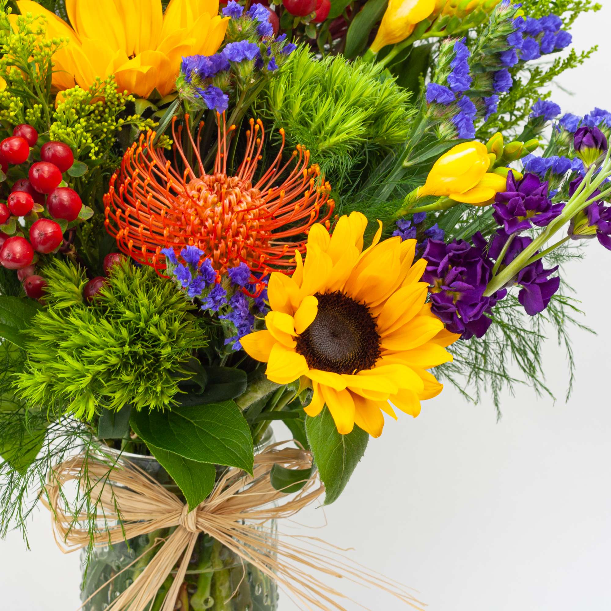 Bright mixed bouquet with sunflowers, purple blooms, and red berries in a glass vase