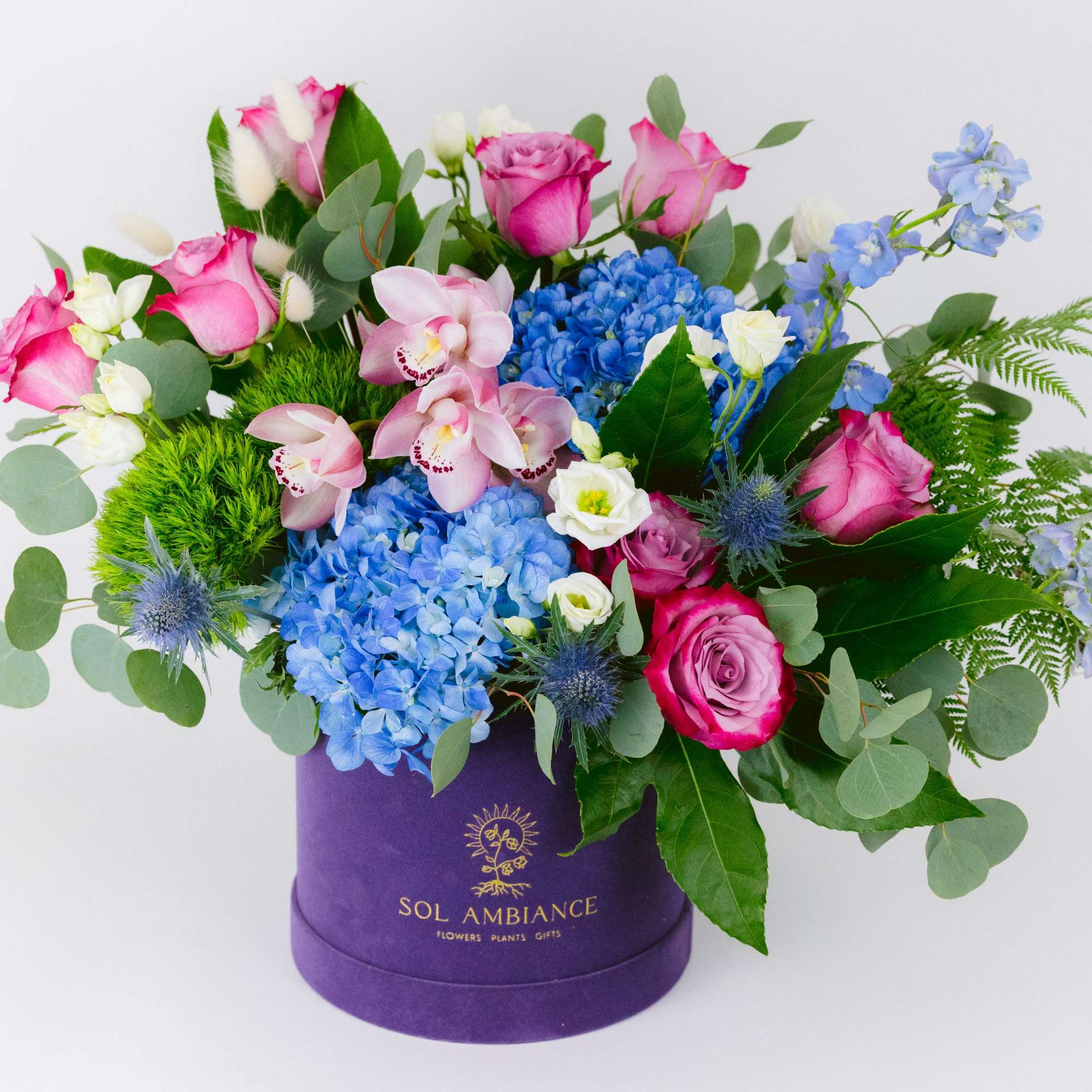 Pink roses and blue hydrangeas in a purple hatbox