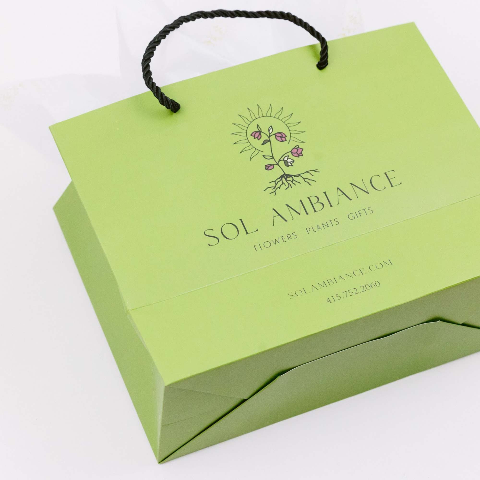 Lime green gift bag with black rope handles and floral logo