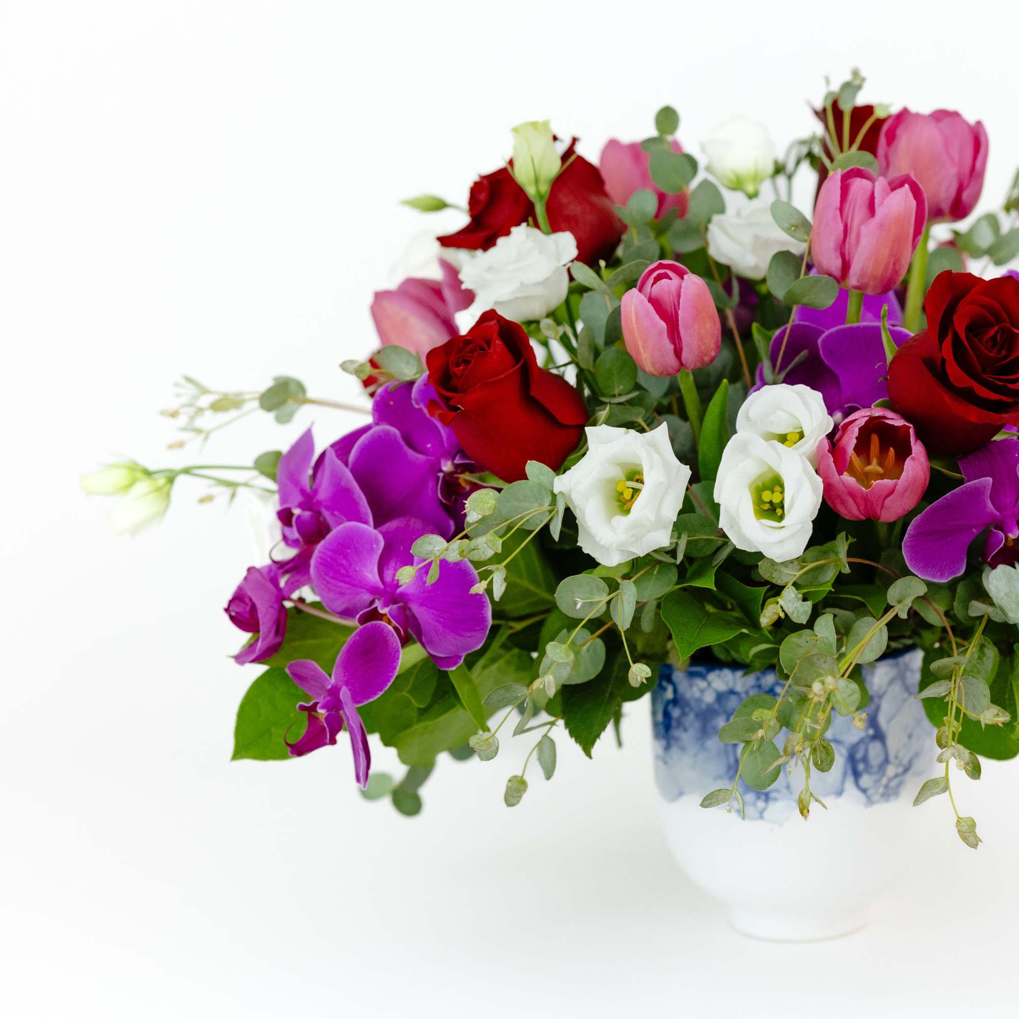 Mixed bouquet of red roses, pink tulips, white blooms, and purple orchids in a blue-and-white vase