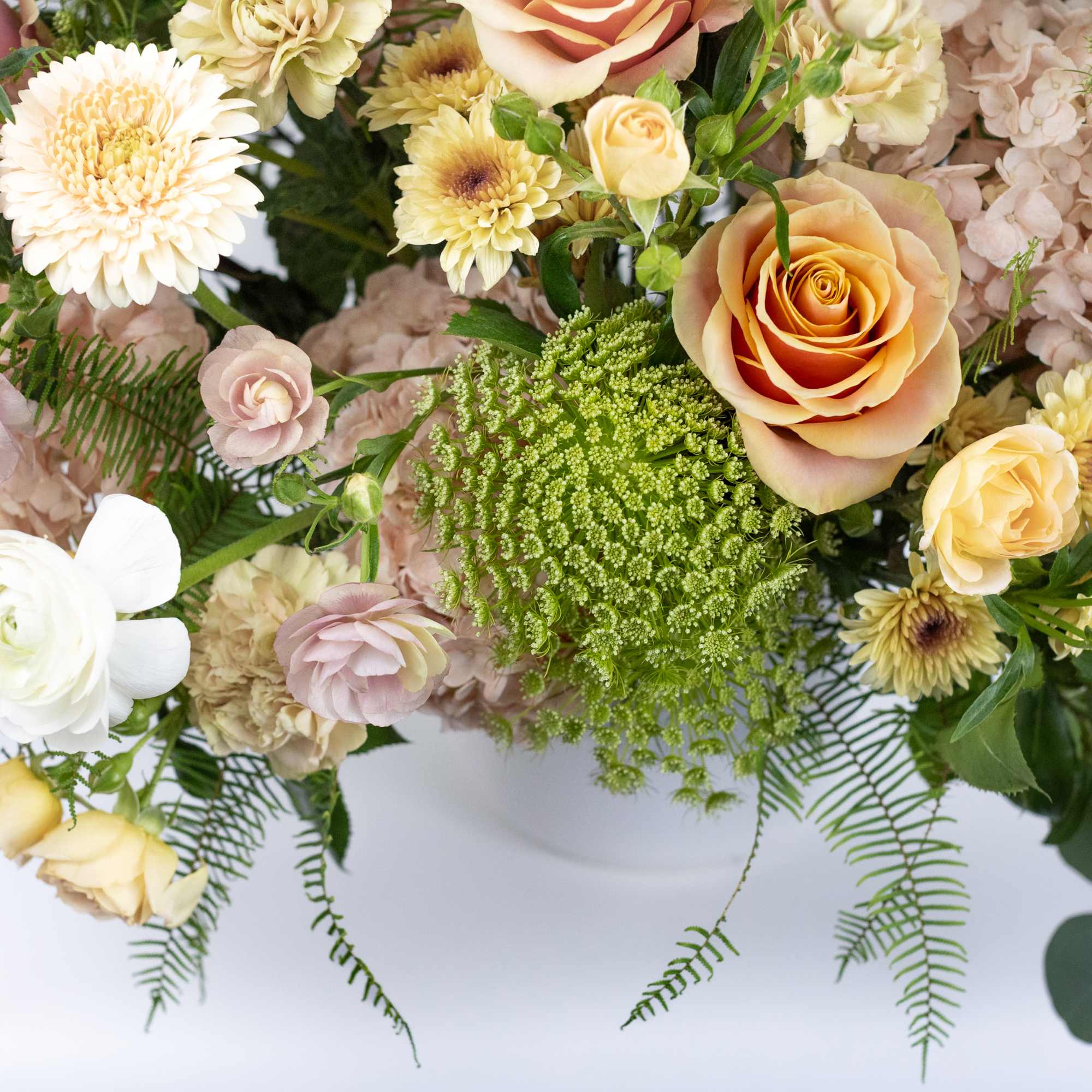 Mixed bouquet of roses, chrysanthemums, and pale blooms in a white vase