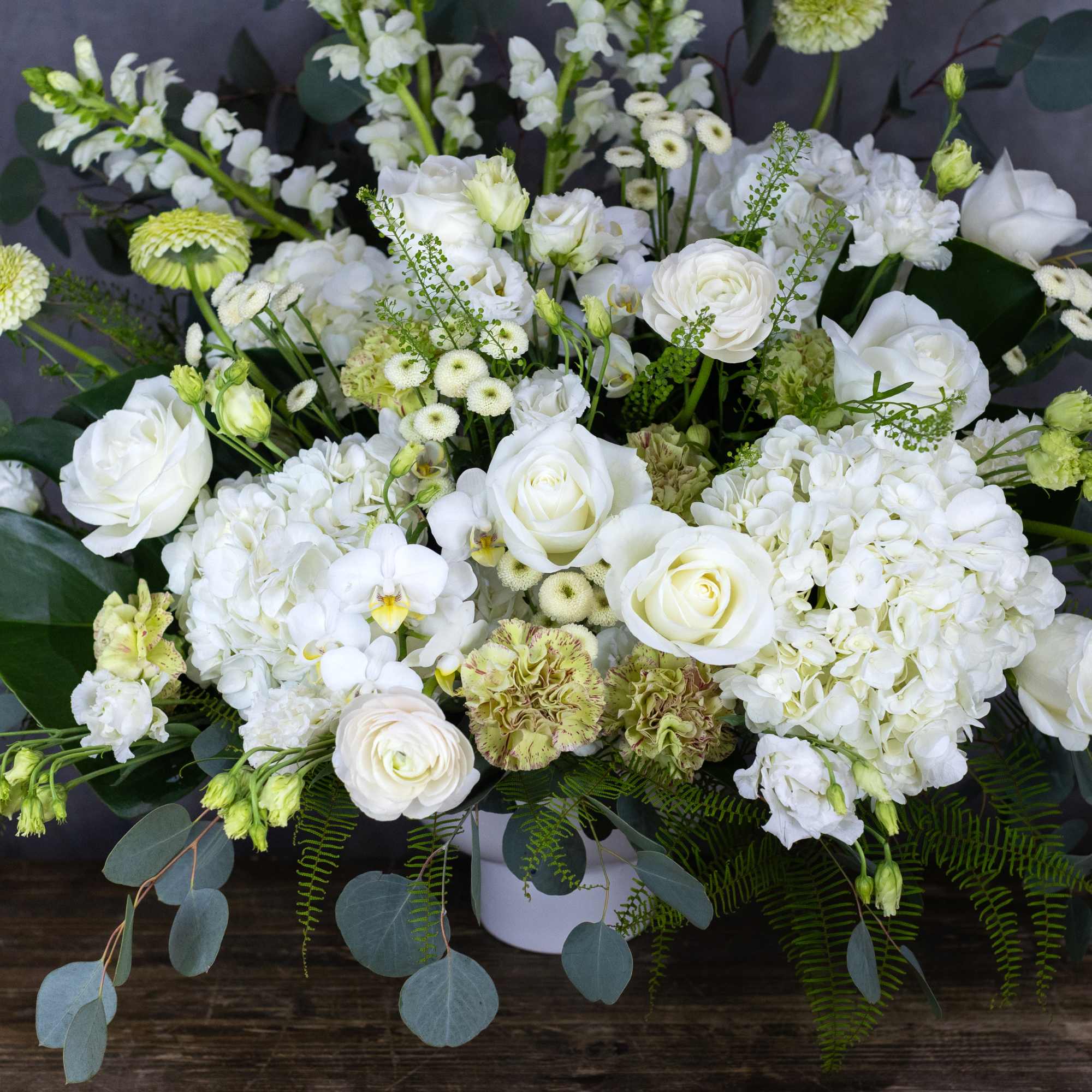 White floral arrangement with roses, hydrangeas, and orchids in a white container