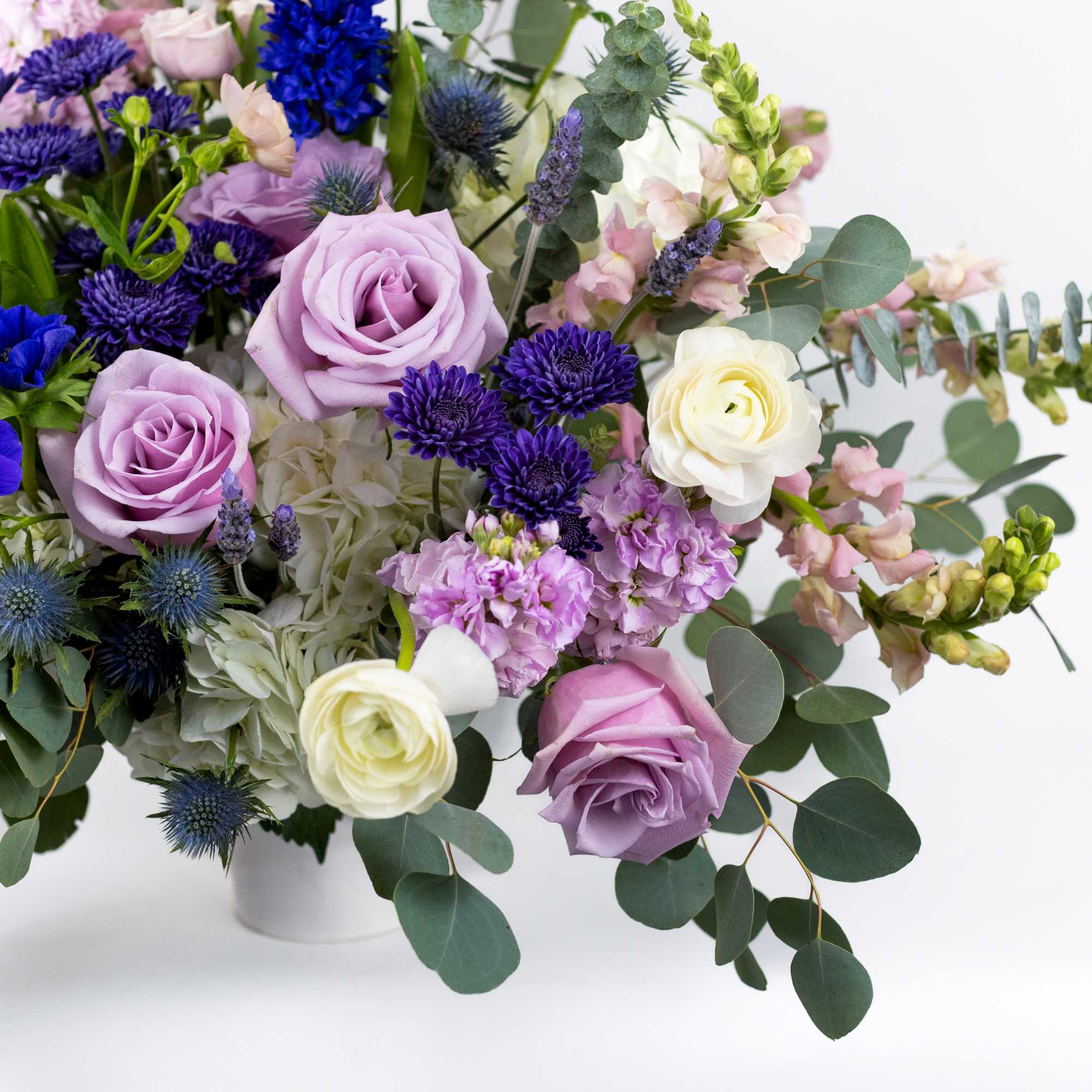 Bouquet of lavender and white roses with blue flowers in a white vase