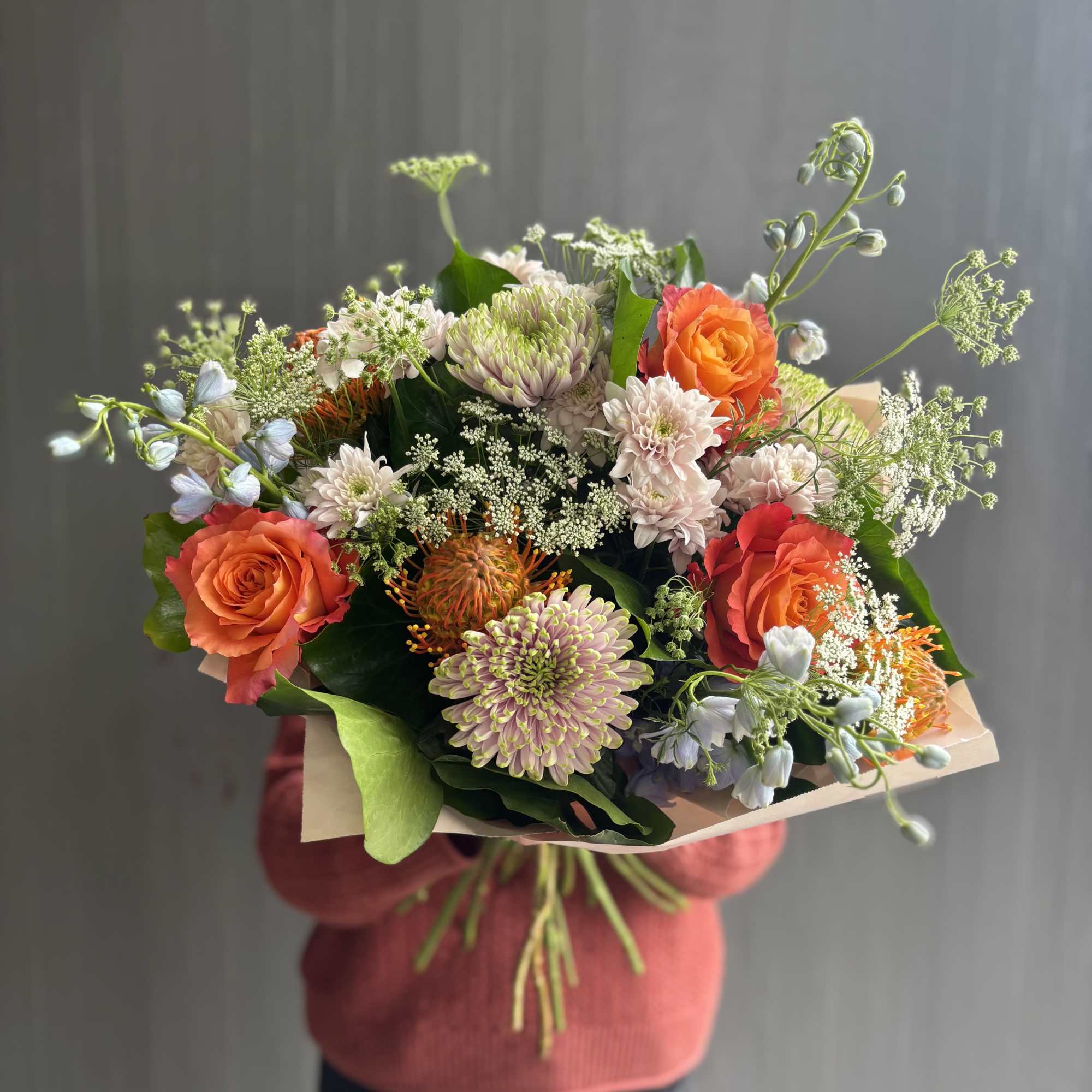 Handheld bouquet of orange roses and pale chrysanthemums with airy filler flowers